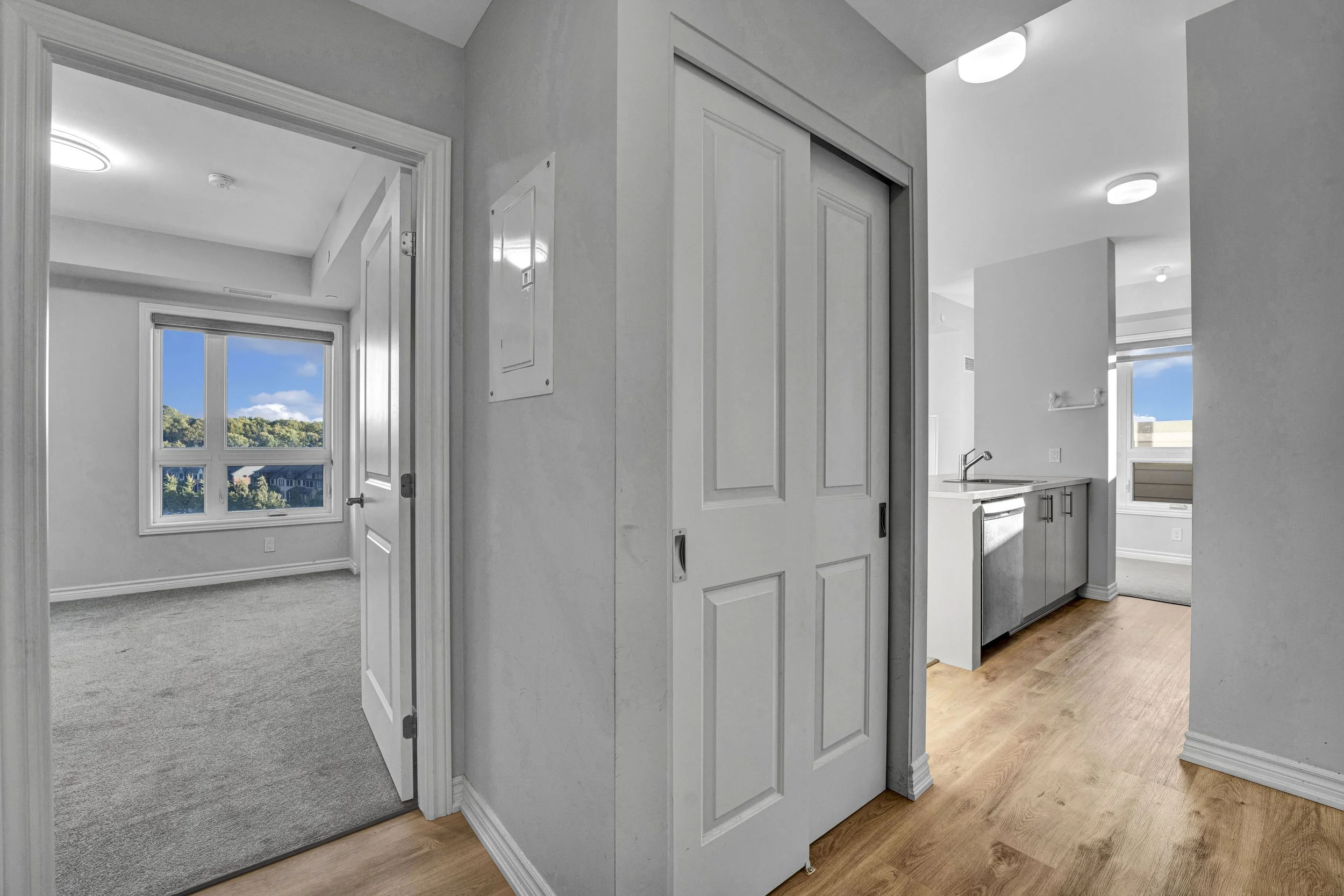 Ottawa Real Estate Photographer NVISION3D.ca  Interior view of an apartment with white walls, a kitchen area with cabinets and a faucet, hardwood flooring, and a window showing a view of greenery and cloudy sky outside.