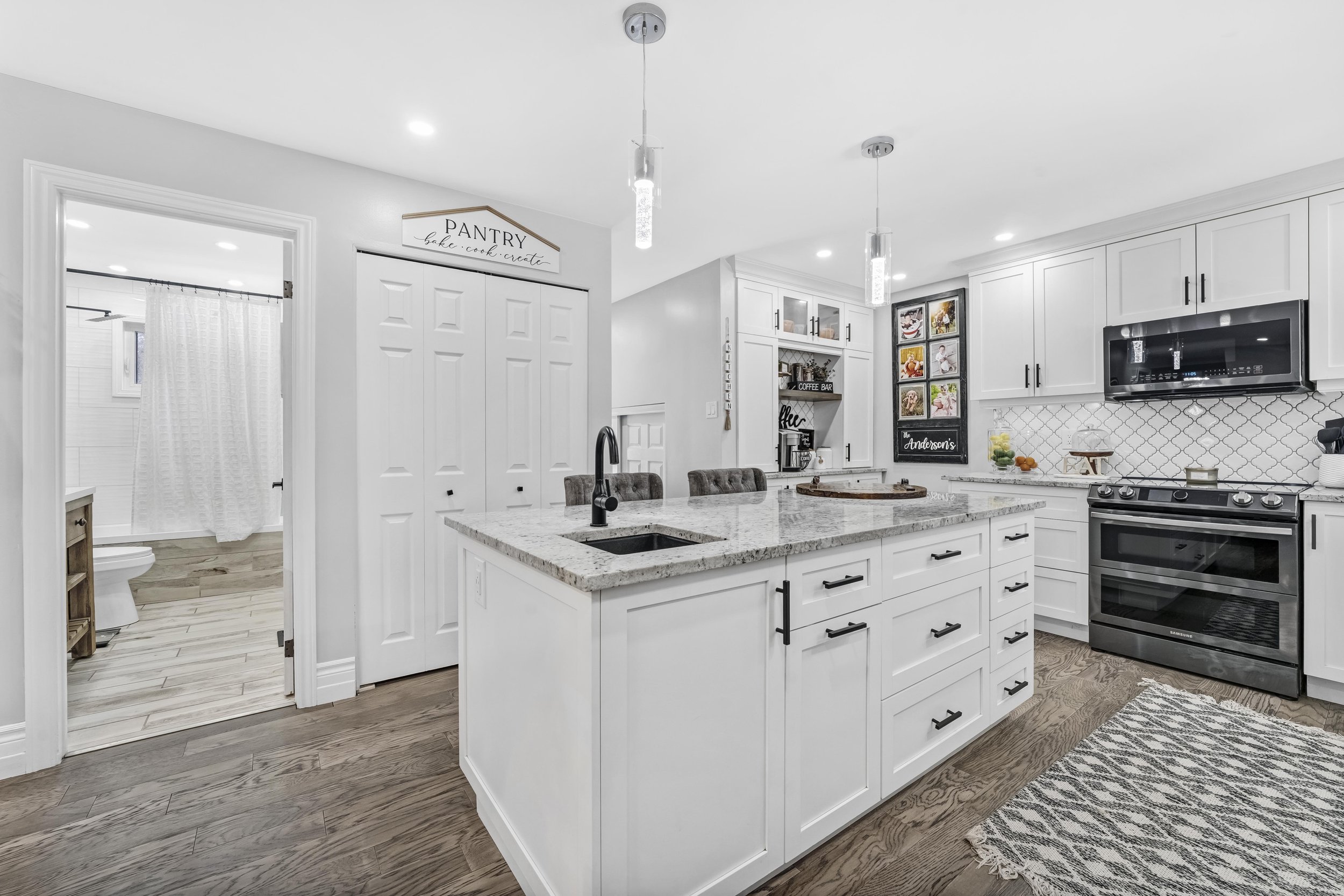 Ottawa Real Estate Photography  Modern kitchen with white cabinets, stainless steel stove and microwave, granite island, hardwood floors, and decorative wall tiles.