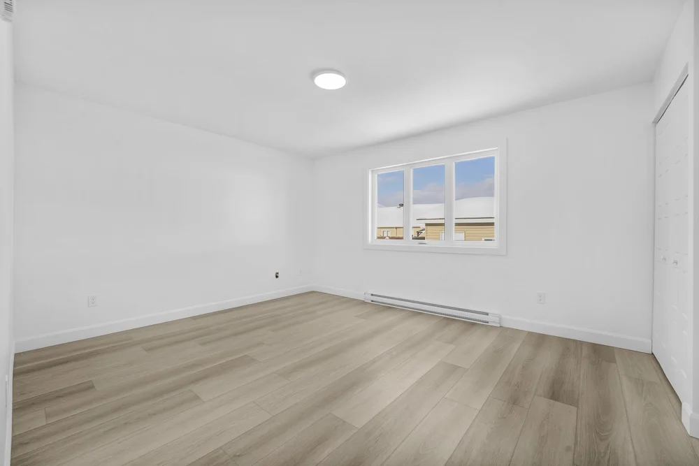 Original photo of a vacant bedroom with white walls, a window and wood flooring
