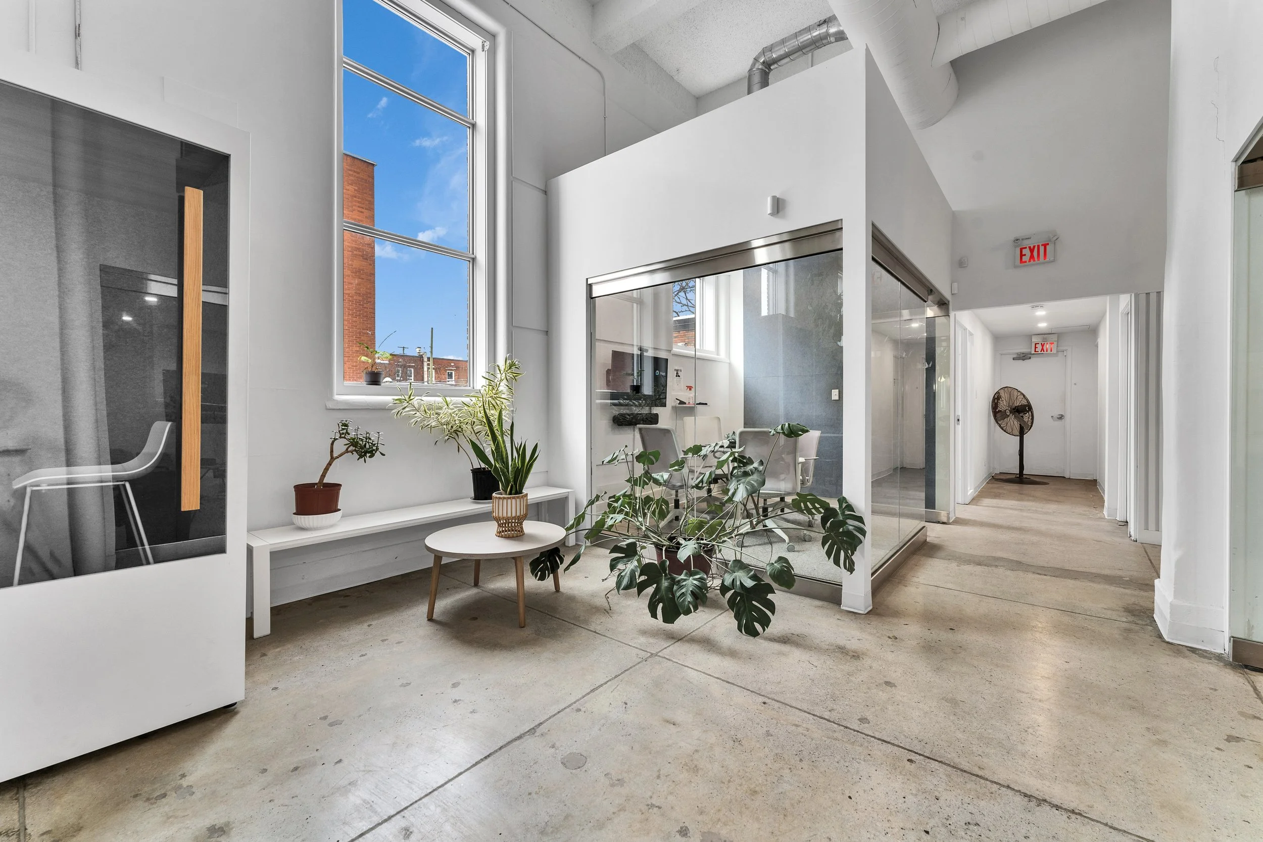photographie immobiliere outaouis  Modern office interior with large window, white walls, concrete floor, indoor plants, and glass-walled conference room.