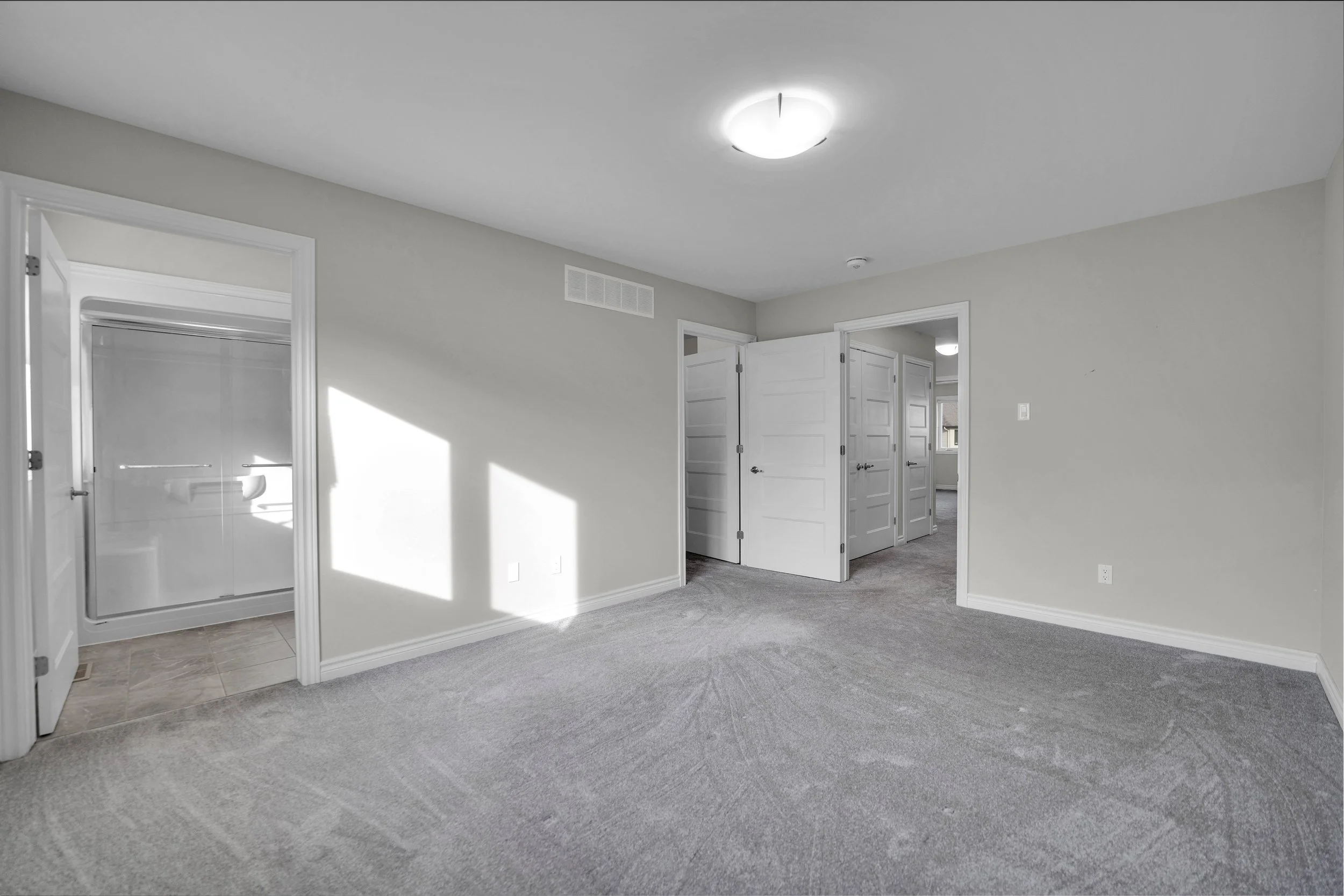 NVISION3D Real Estate Photography Ottawa  Empty room with gray carpet, open doors leading to a bathroom and another room, ceiling light, and a wall vent.