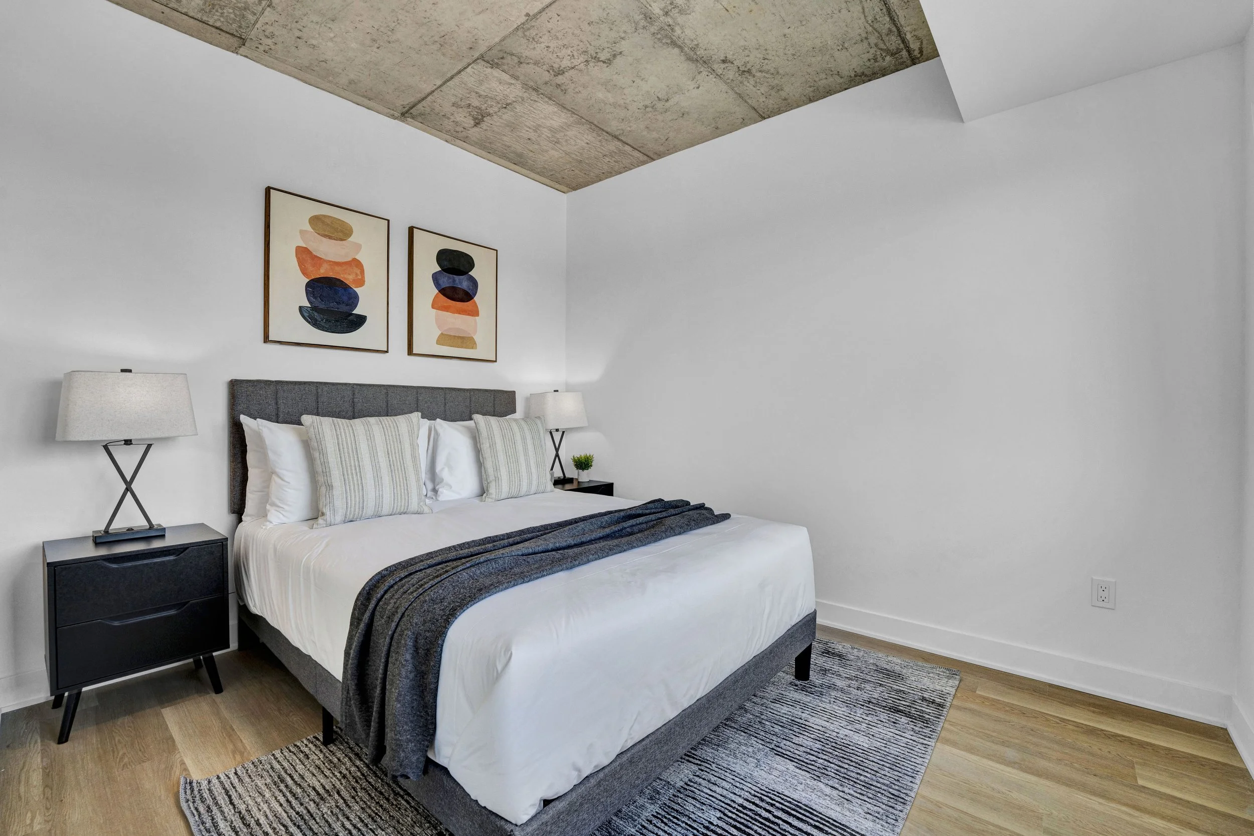 Ottawa Real Estate Photographer A modern bedroom with a bed, nightstand, and lamps, decorated with abstract artwork on the white wall and a textured ceiling.