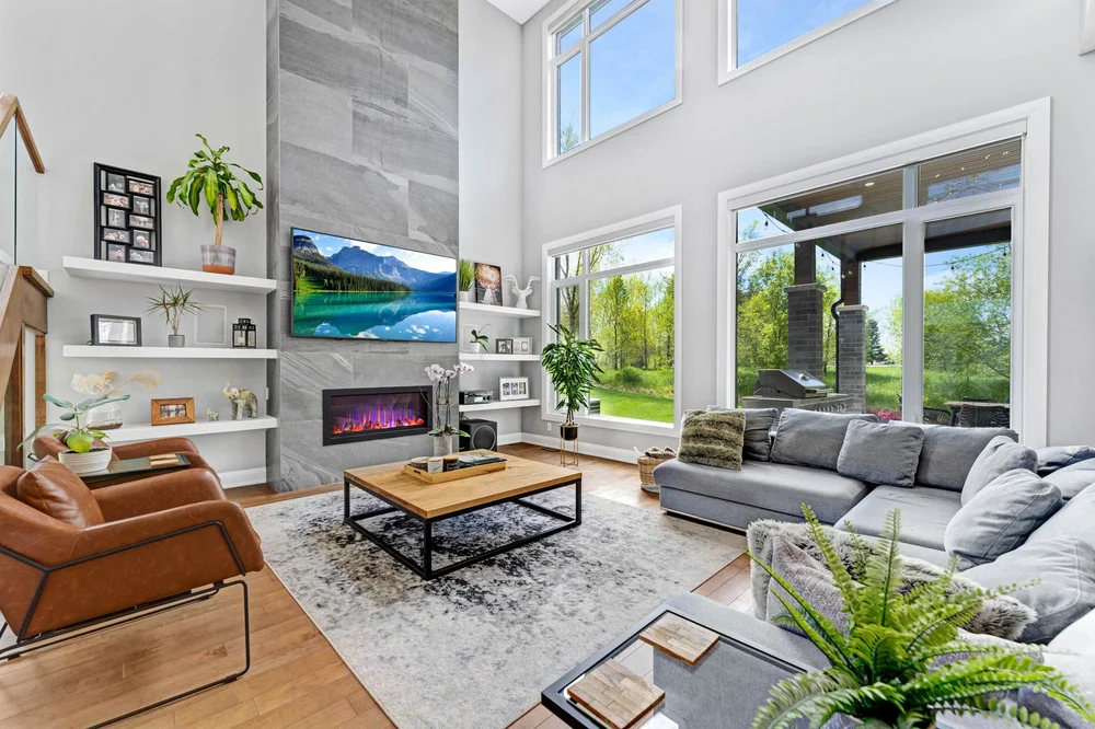 Double-height living room with tall windows, a fireplace and tan armchairs