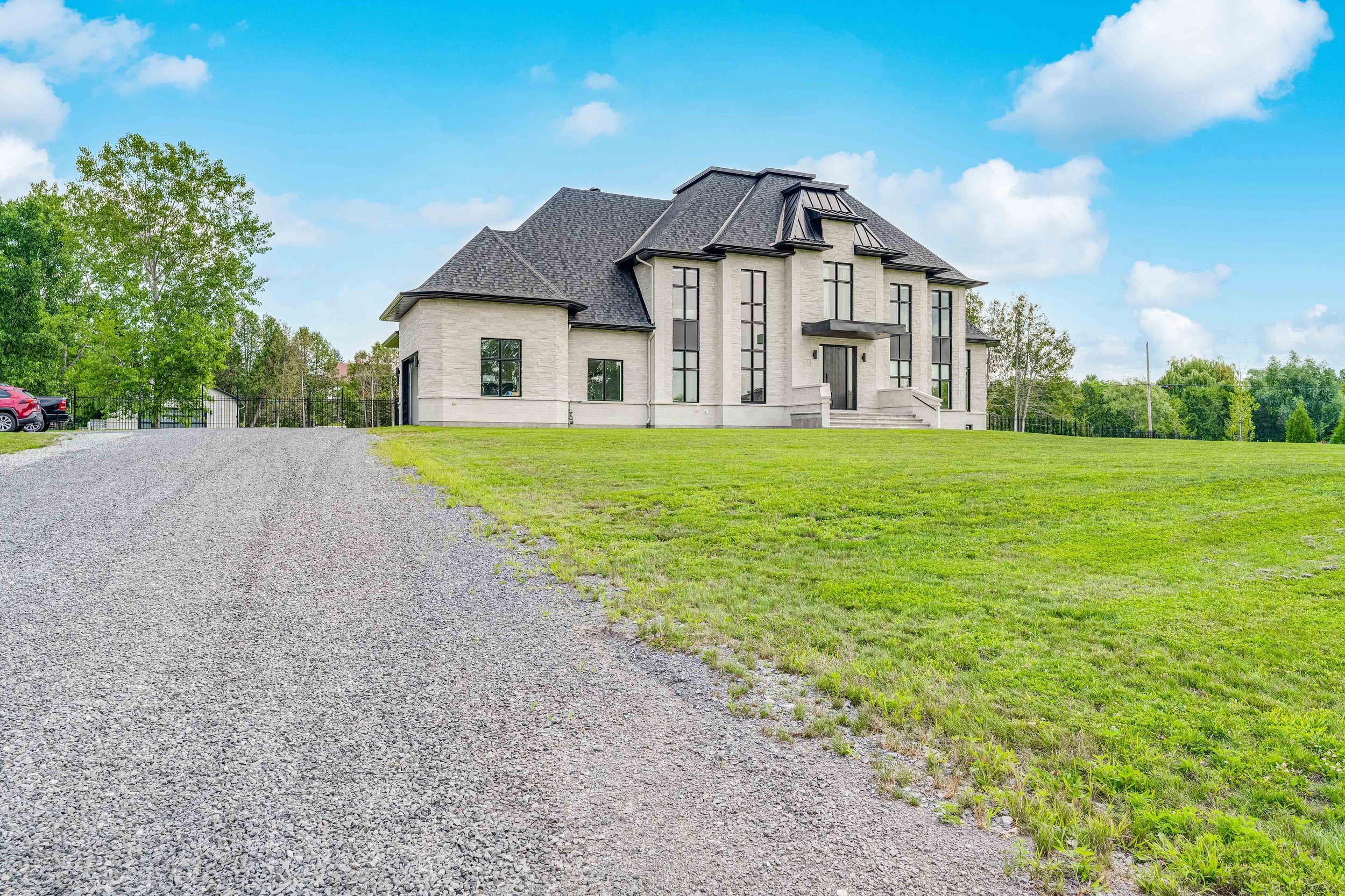 Large modern house with gray roof, wide driveway, and green lawn under blue sky.