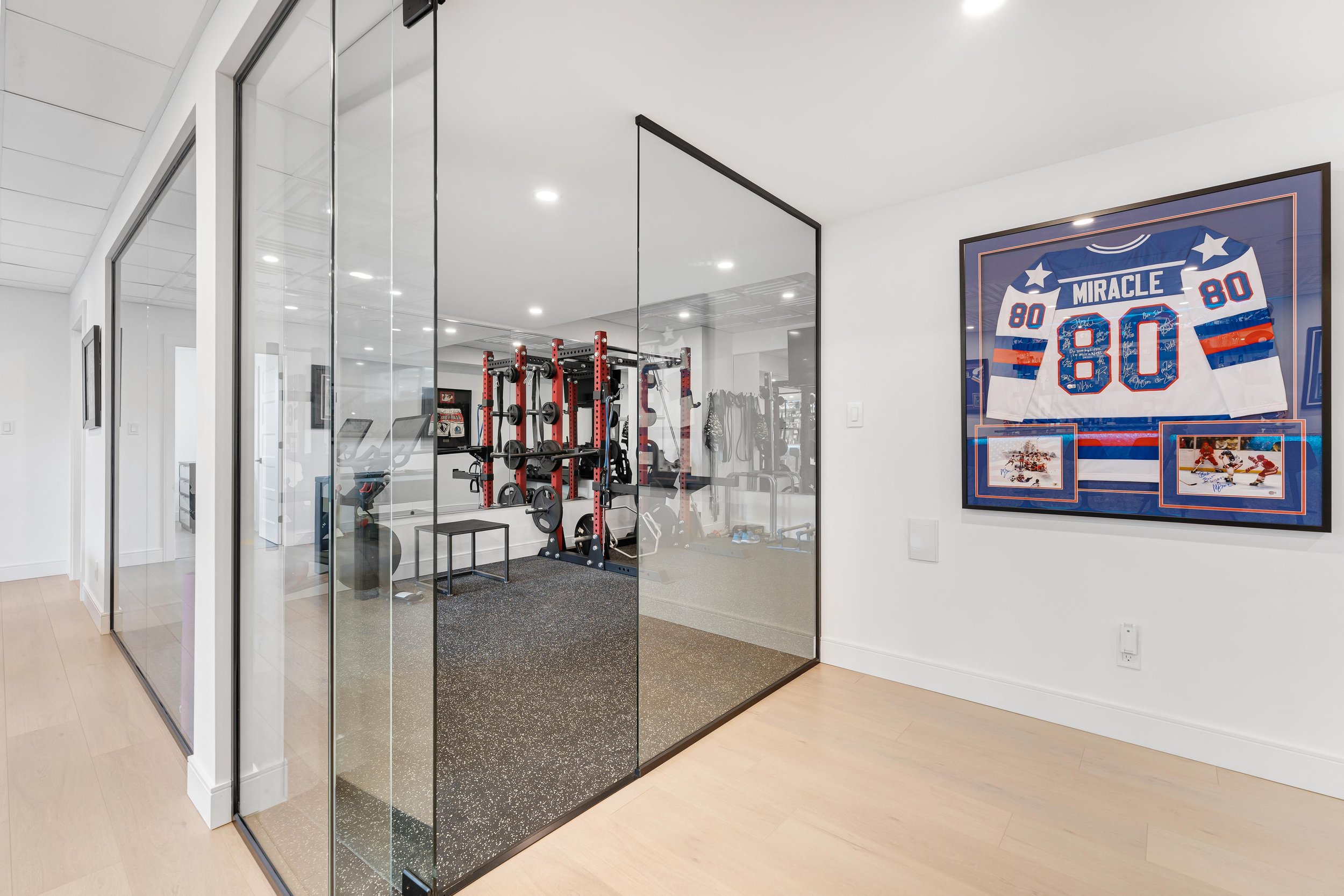 Home gym with fitness equipment, glass doors, and framed sports jersey on the wall.