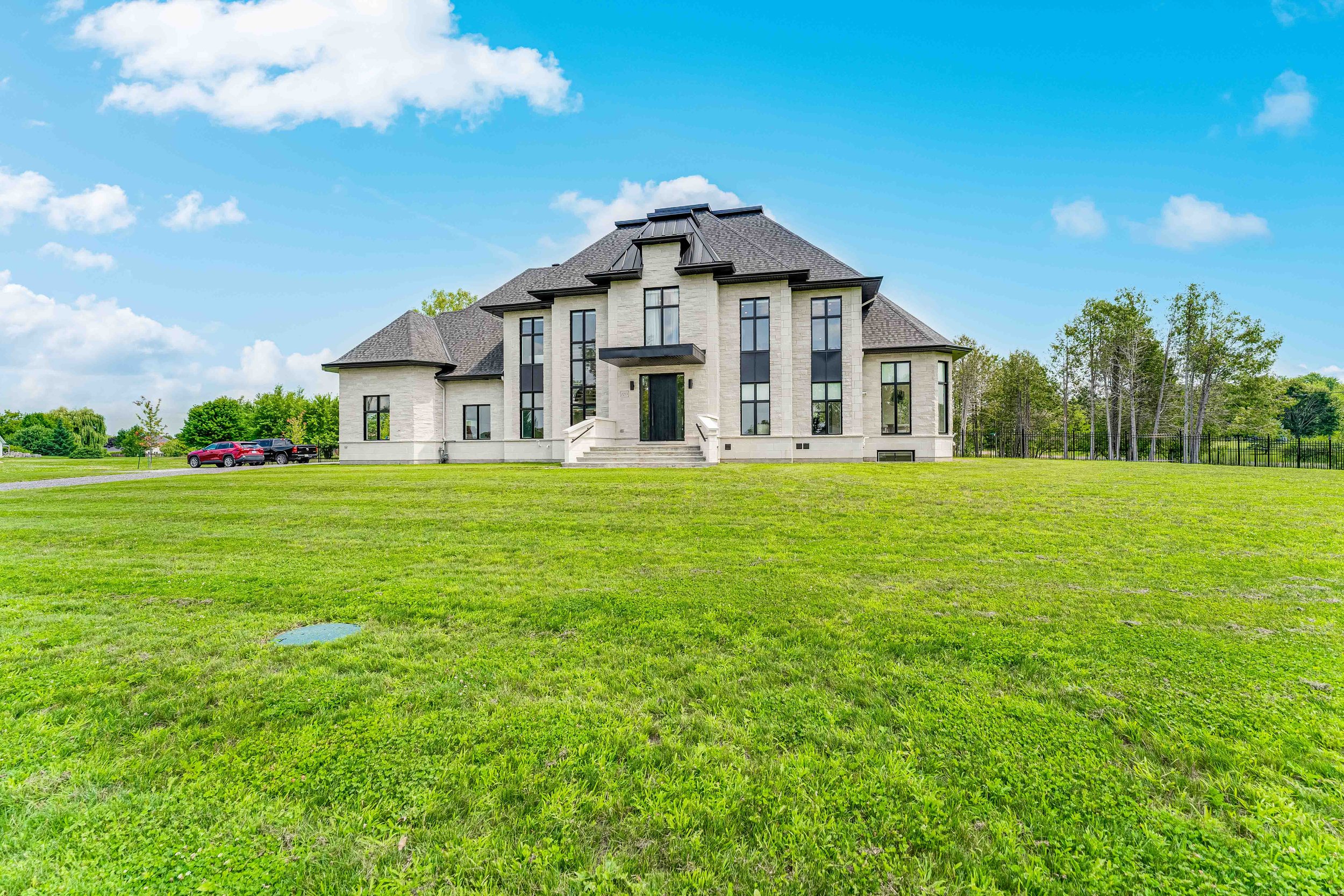 Large modern house with a dark roof, multiple windows, and a front porch set in a spacious green lawn with blue skies.