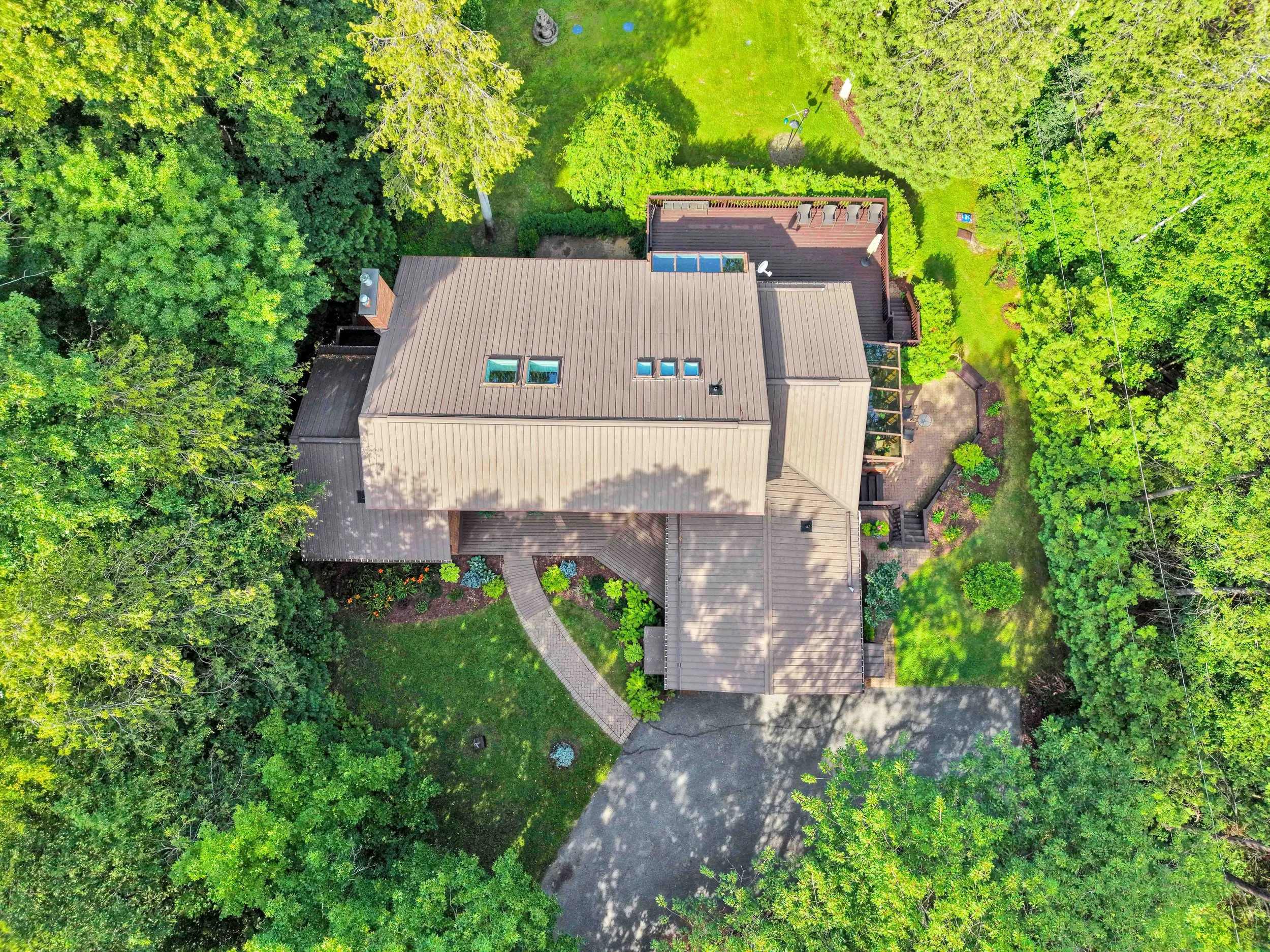 NVISION 3D Real Estate Media  An aerial view of a house with a brown roof surrounded by lush green trees and a well-maintained garden.