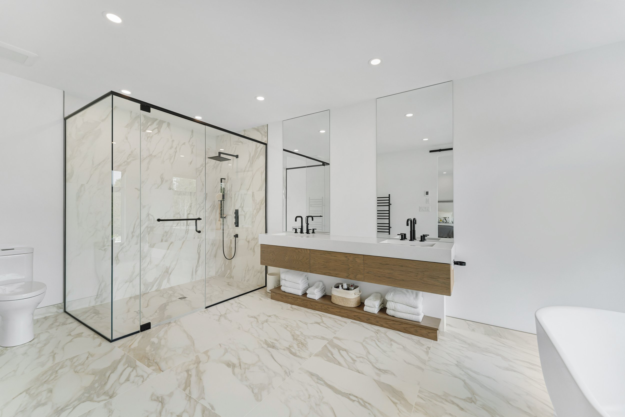 Modern bathroom with a glass-enclosed shower, double vanity with two sinks, large mirror, and a freestanding bathtub on marble flooring. Real estate photography ottawa