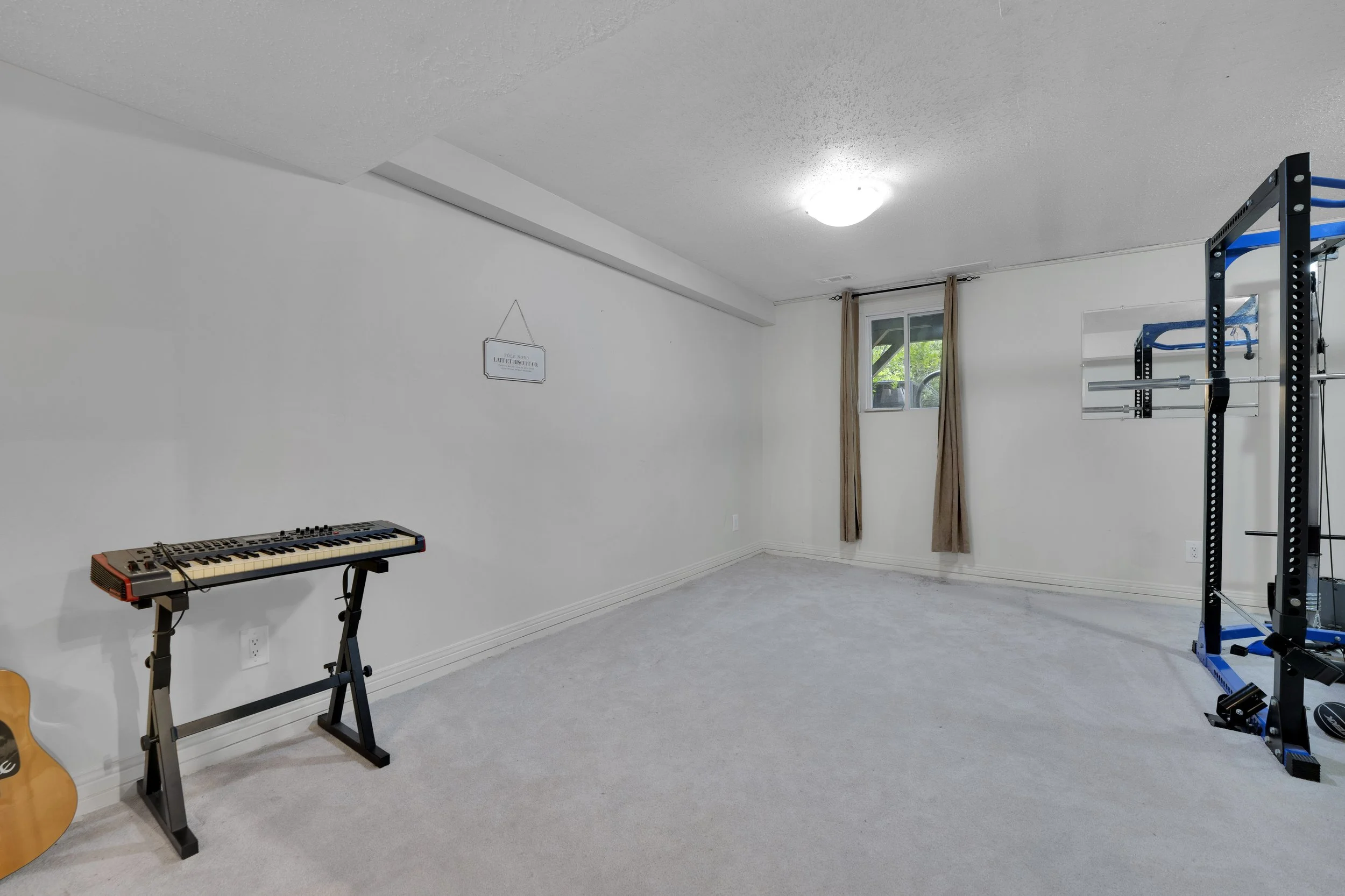 NVISION3D Real Estate Photography Ottawa  Room with white walls and ceiling, gray carpet, window with beige curtains, a keyboard on a stand, and gym equipment including a squat rack with a barbell.