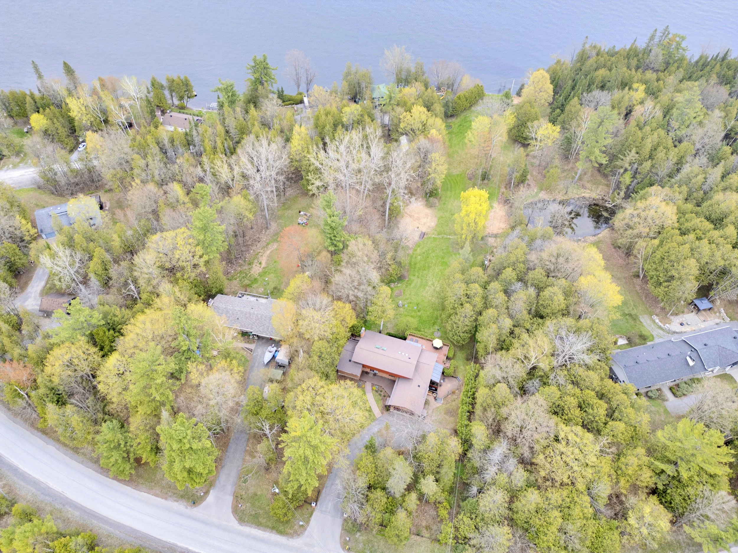 Ottawa Real Estate Media Services  An aerial view of a residential neighborhood with houses surrounded by lush green and yellow trees, next to a large body of water, with a curved street in the foreground.