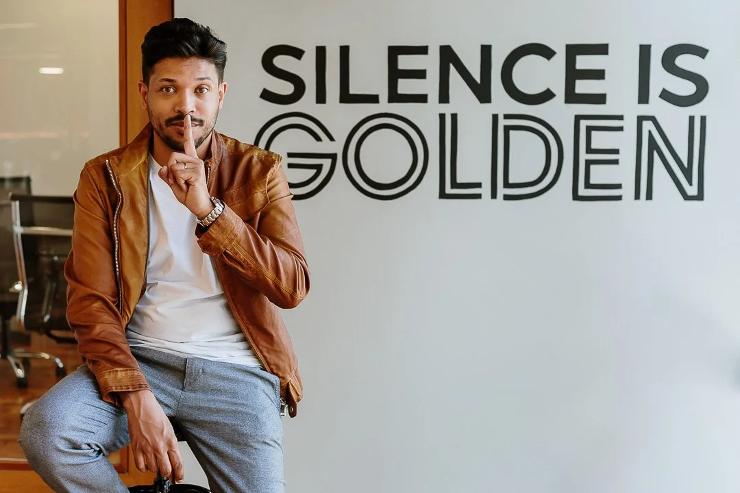 A man with a finger to his lips, standing in front of a wall with the words 'Silence Is Golden'.