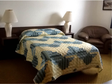 Eagle Plains Hotel, room with double bed, patterned quilt bedspread, two white lamps on either side of bed, comfy chair in corner