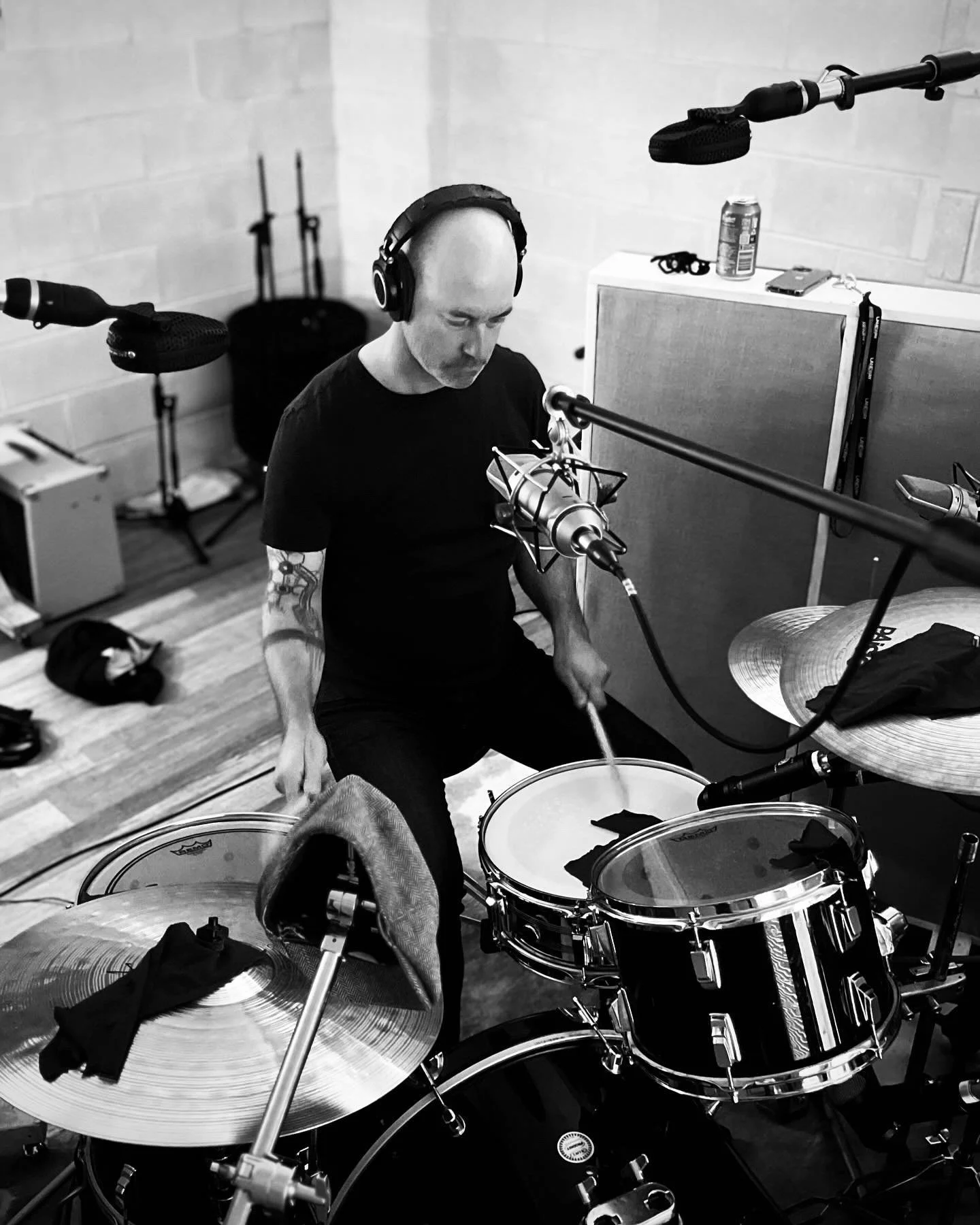 Paul Francis Wood recording a man with a tattooed arm wearing headphones, sitting behind a drum set with cymbals, in the recording studio based in Perth Western australia