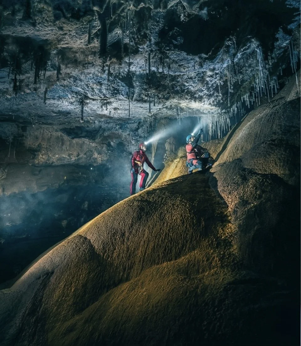 Two cavers pick their way across a flowstone dome, headlamps cutting through the mist toward a ceiling draped in frost-white formations, Kubla Khan Cave, Mole Creek Karst National Park, Tasmania.