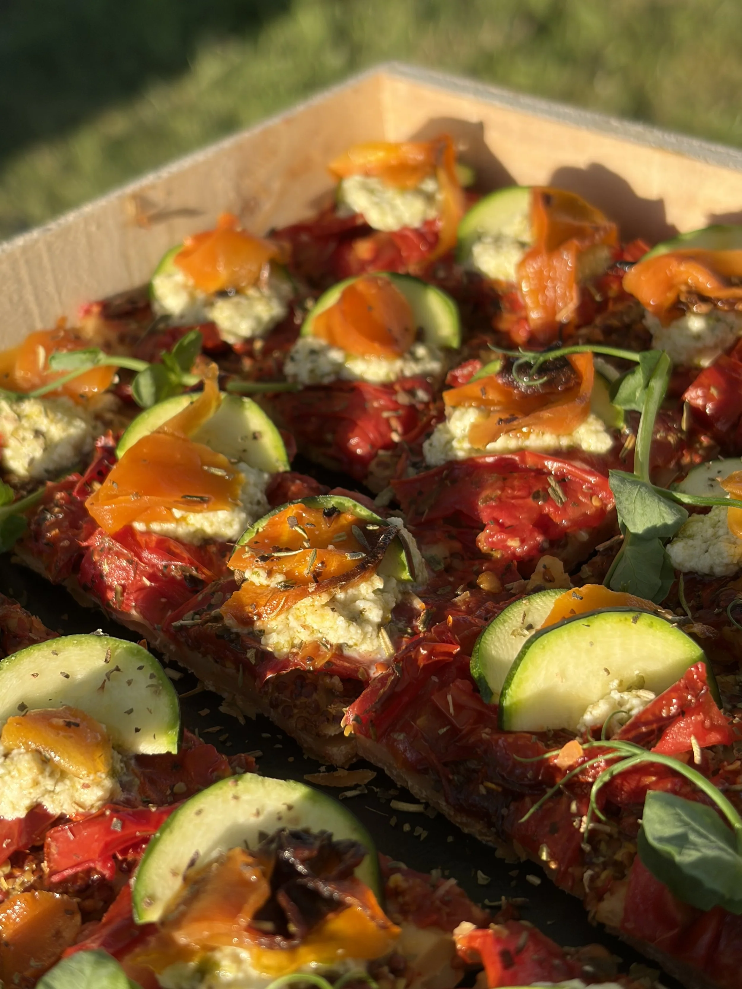 Une tarte salée garnie de légumes, de fromage, avec des rondelles de courgette, des poivrons rouges et orange, et des herbes fraîches.