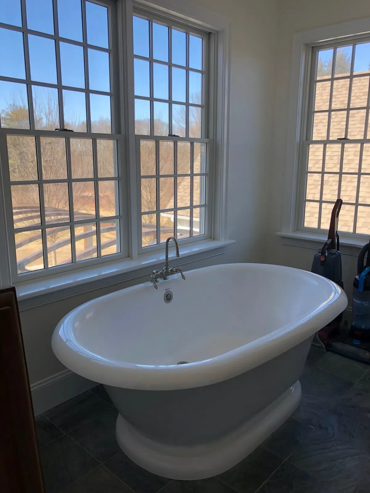 A white freestanding bathtub near large windows with a scenic outdoor view in a bright bathroom. west newbury
