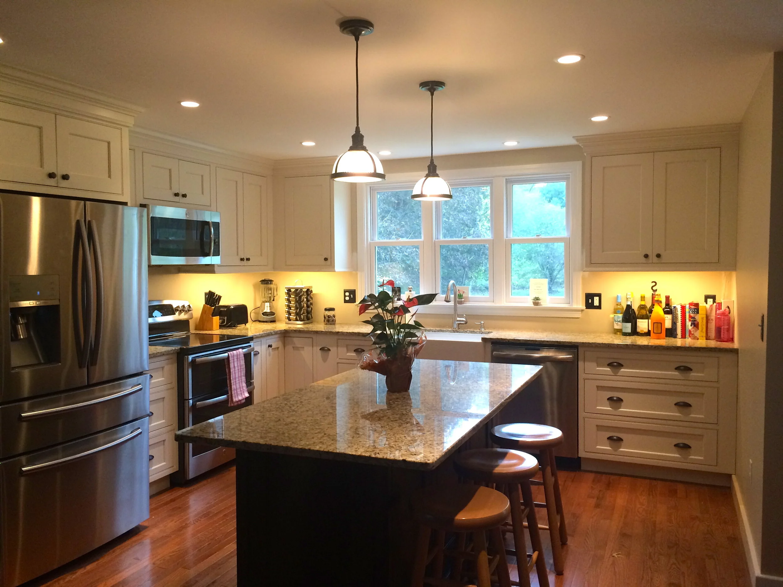 A modern Newburyport kitchen with white cabinetry, stainless steel appliances, granite countertops, a central island with wooden stools.. There are pendant lights hanging over the island and recessed lighting in the ceiling.