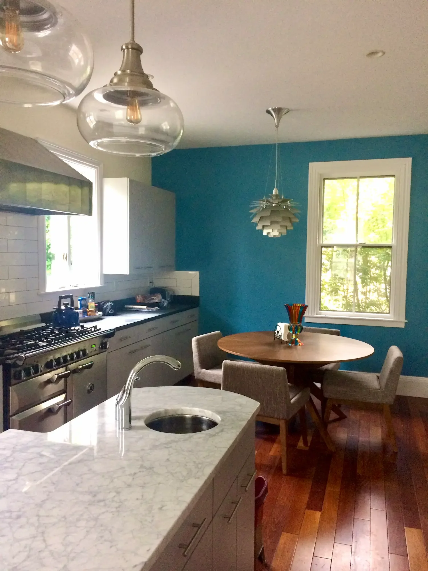 Open plan kitchen remodel with gray island, marble countertops, professional range, stone backsplash, and custom range hood — North Shore, MA