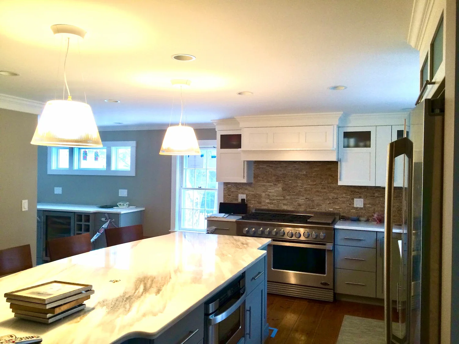 Open plan kitchen and dining remodel with gray cabinets, marble island, teal accent wall, globe pendant lighting, and professional range — Newburyport, MA