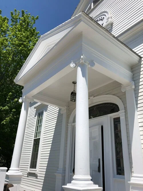 Hampton Falls church entrance with columns, front door, arched window, and a hanging lantern, under a small roofed porch