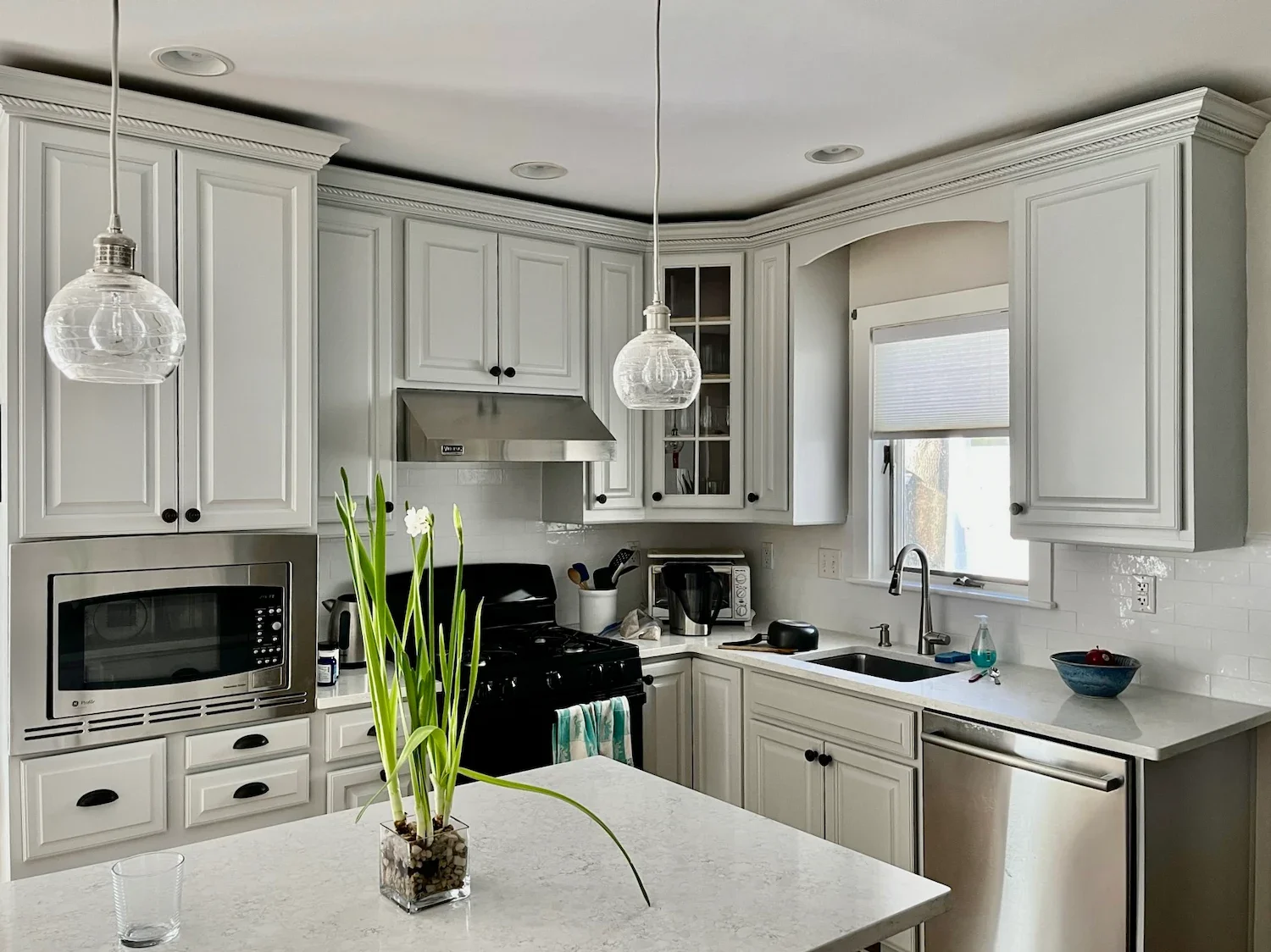 Kitchen cabinet painting with light gray finish, crown molding, quartz countertops, and glass globe pendant lighting — North Shore, MA