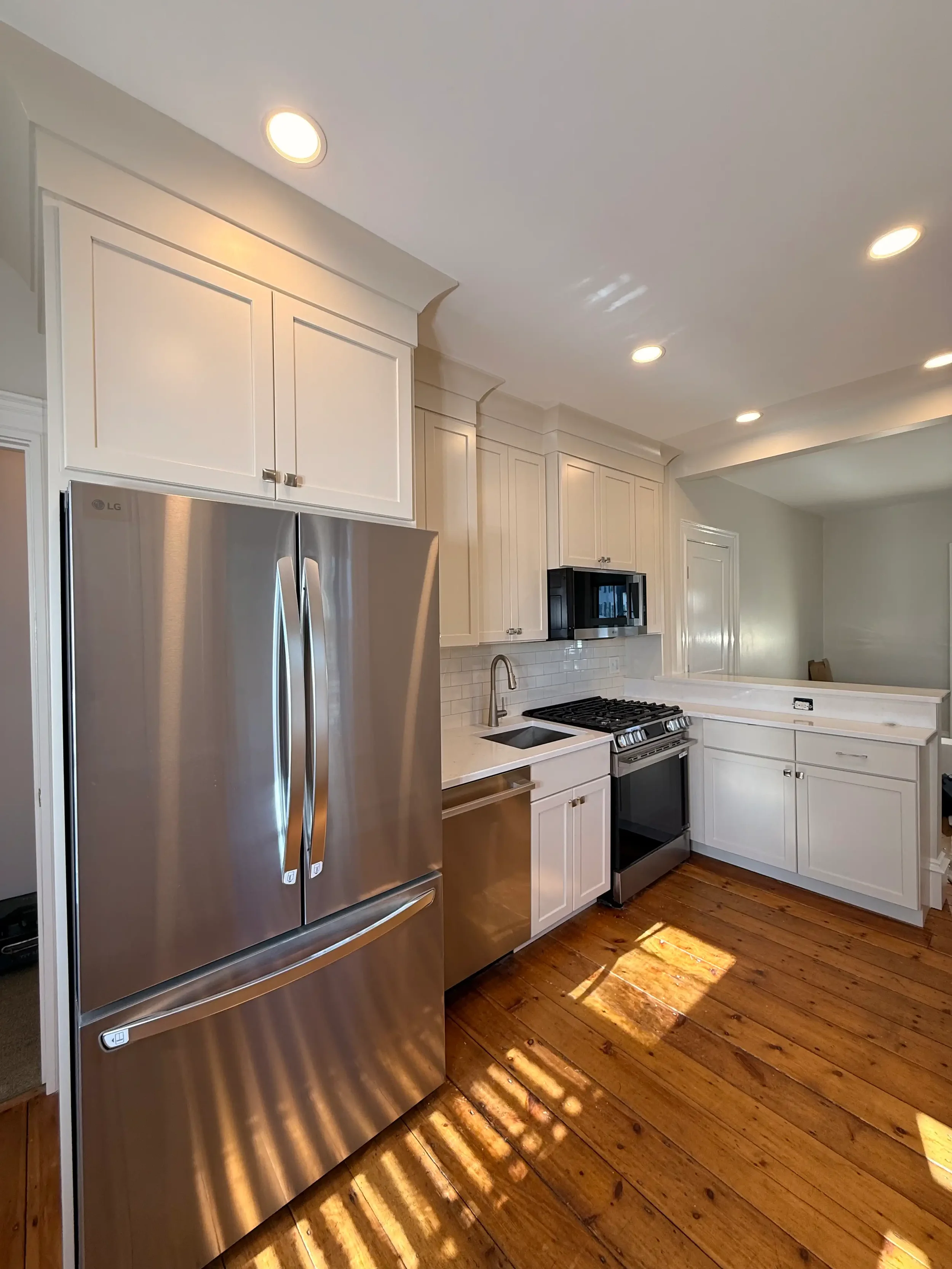 Kitchen renovation with tall white shaker cabinets, subway tile backsplash, stainless steel appliances, and original pine hardwood floors — Newburyport, MA