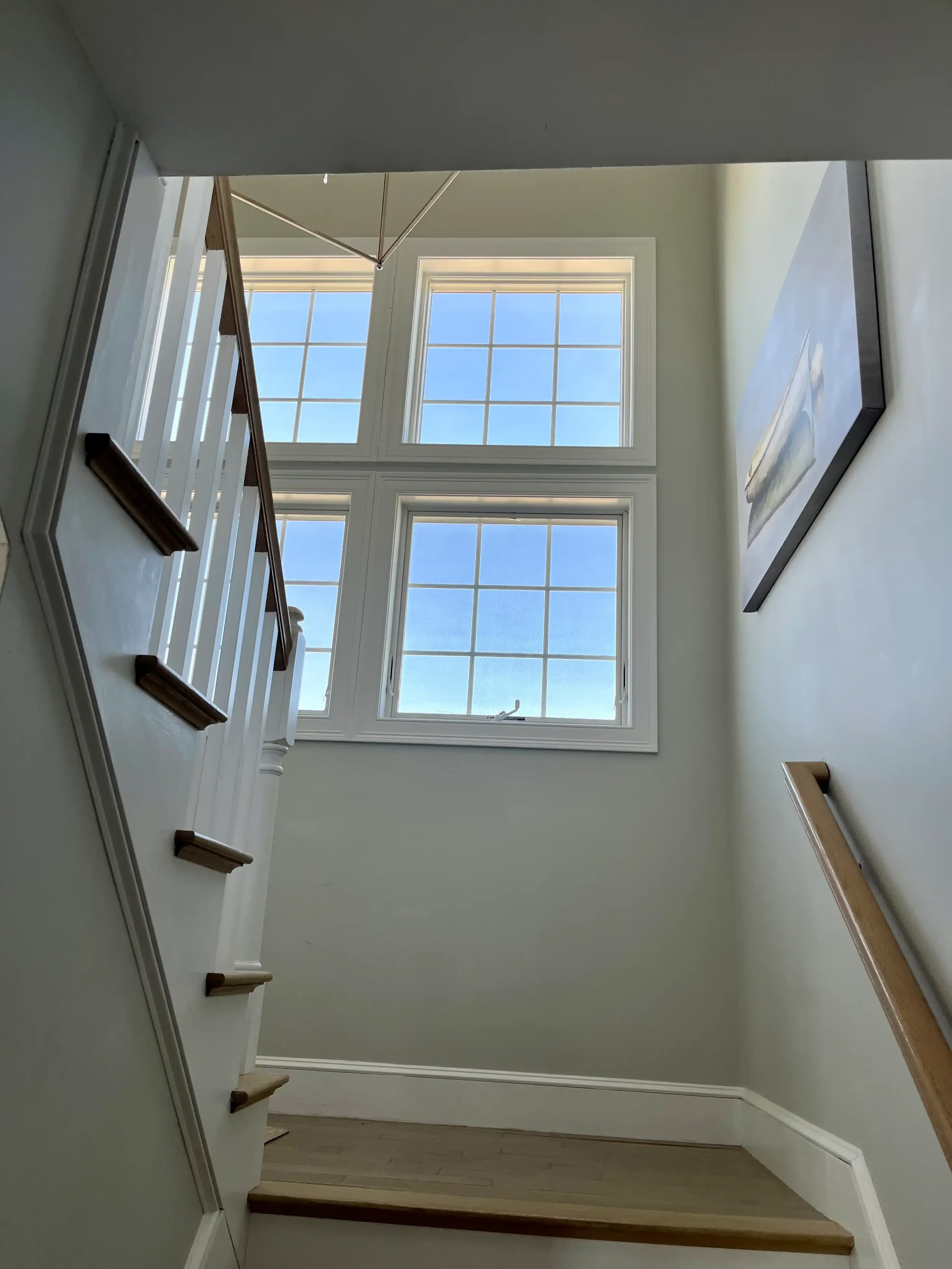 Interior painting of a double-height staircase with painted white balusters, trim, and large grid windows — Newburyport, MA