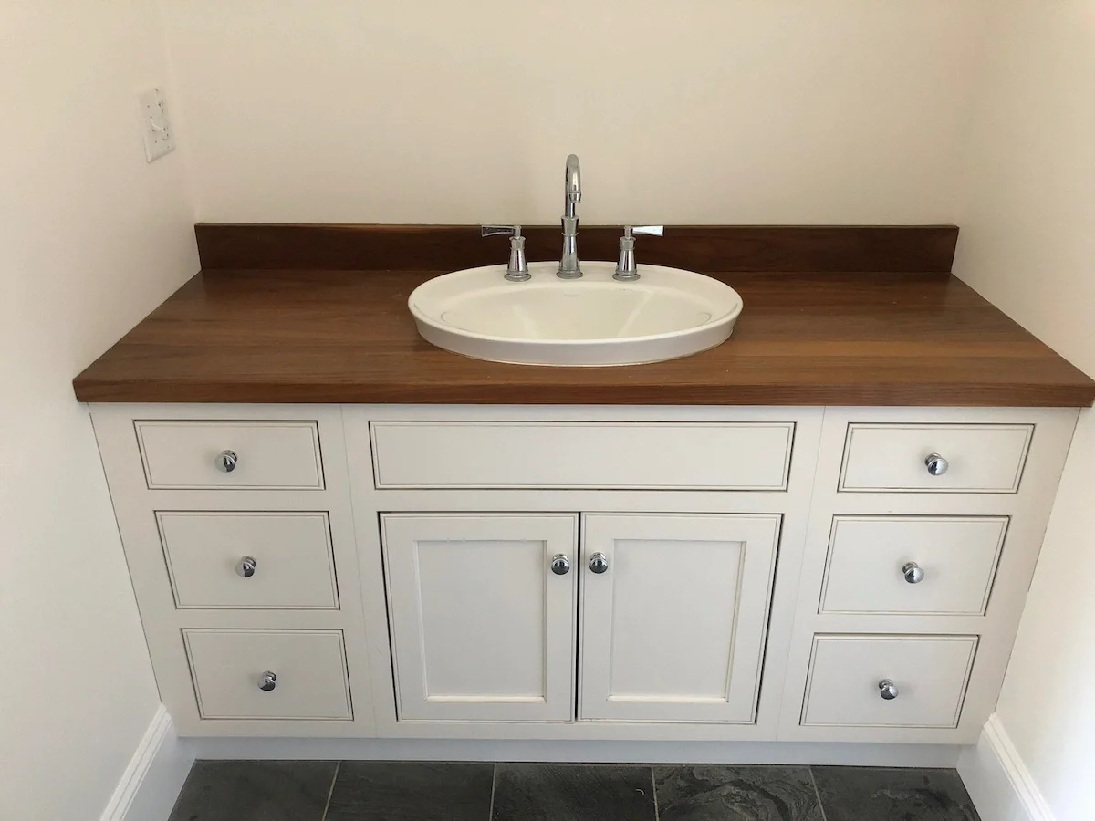 Bathroom vanity with white cabinet, wooden countertop, oval sink, and chrome faucet and knobs.