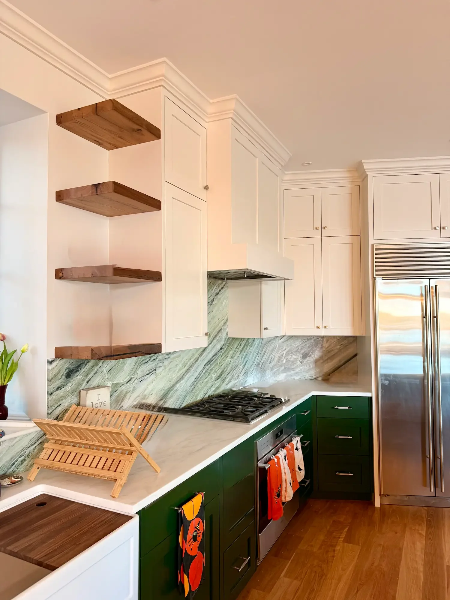 Two-tone kitchen remodel with hunter green lower cabinets, white shaker uppers, green marble backsplash, and floating walnut shelves — North Shore, MA