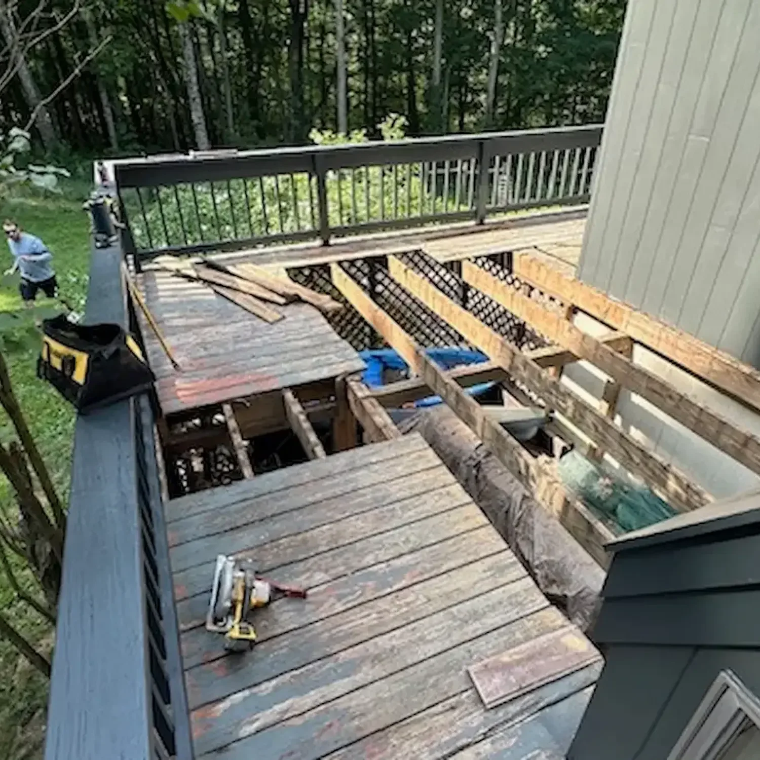 Image of a house deck remodel in amesbury MA, with wooden planks, tools, and construction materials scattered on the floor, and scaffolding on one side.