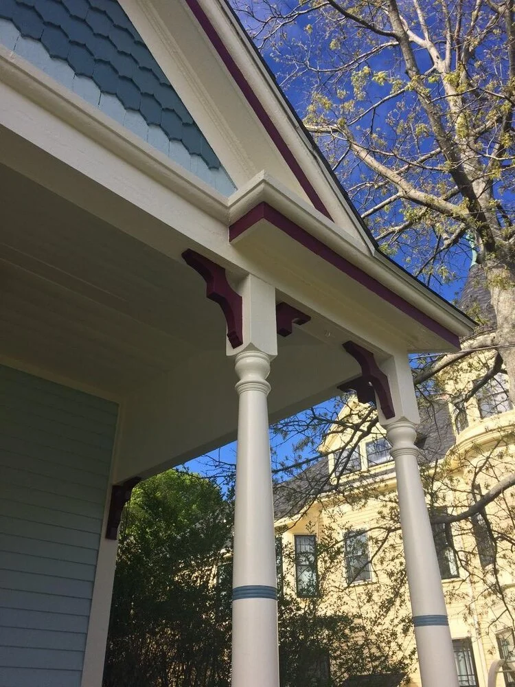 Close-up of the front porch of a Newbury house with white columns, purple decorative accents, intricate trim historic restored