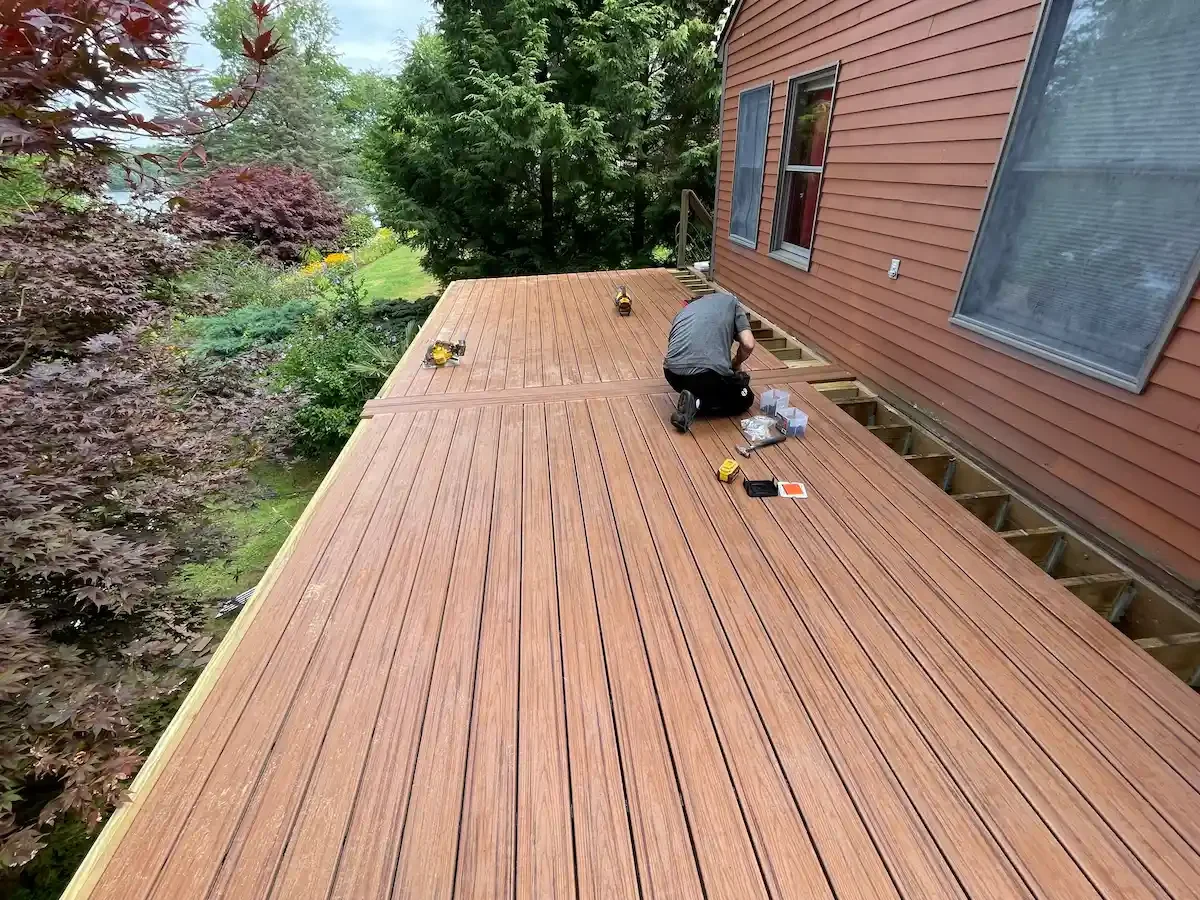 A person working on installing a new wooden deck in Newbury MA  outside a house, with tools and materials scattered around.