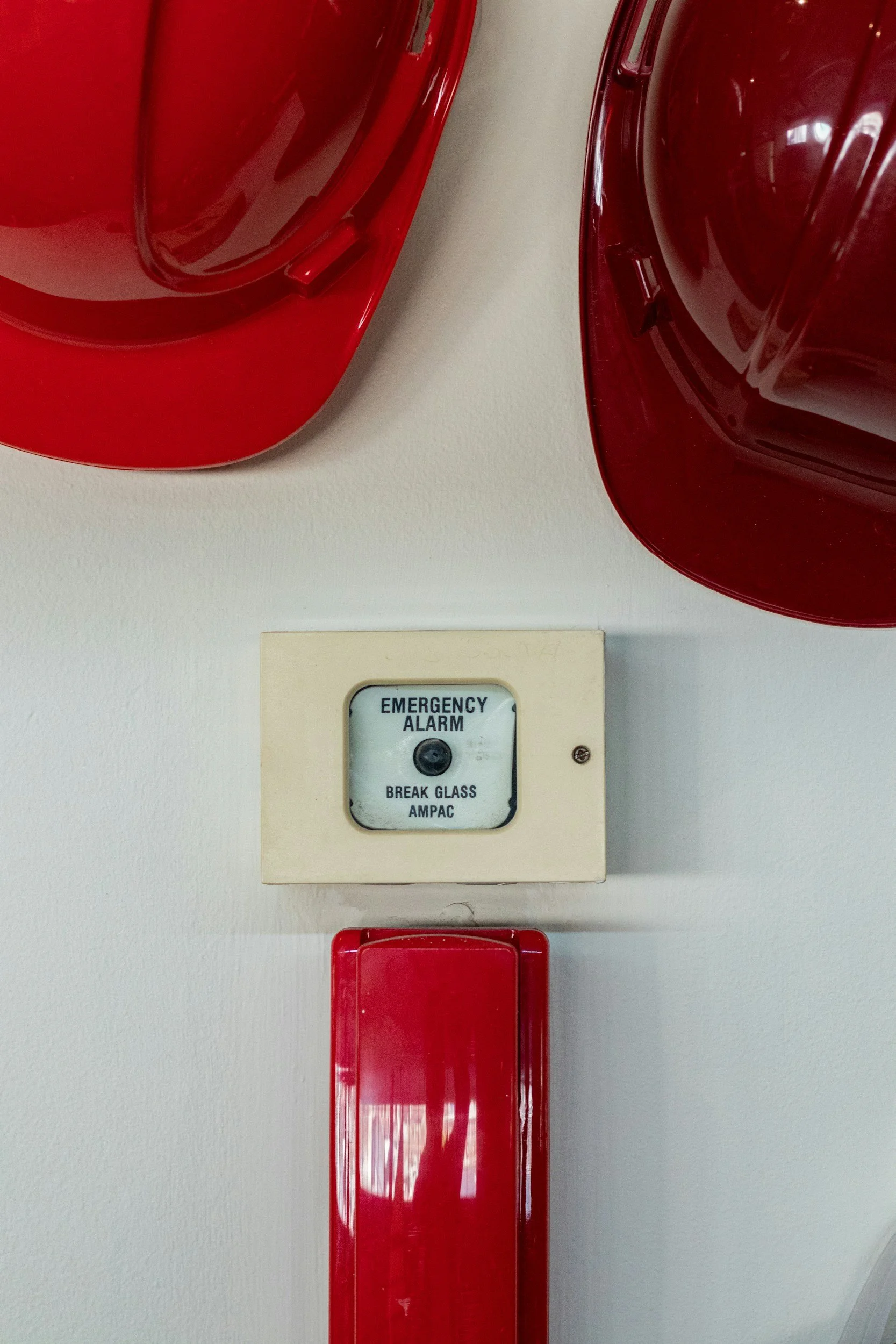 A fire alarm system on a white wall with red fire alarm bells positioned above and below it.