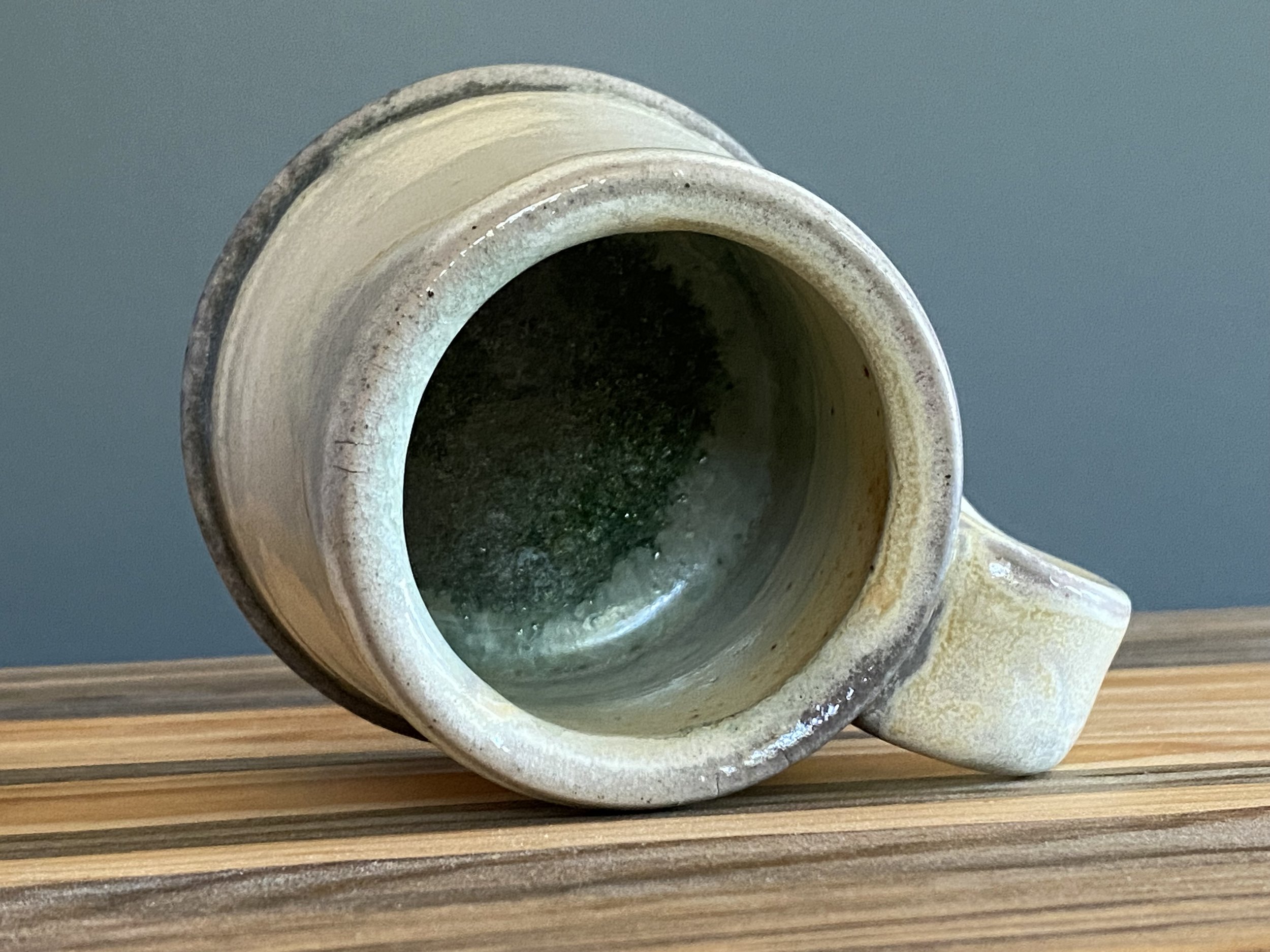 Stoneware mug with yellow salt glaze and green soda glass buildup in interior