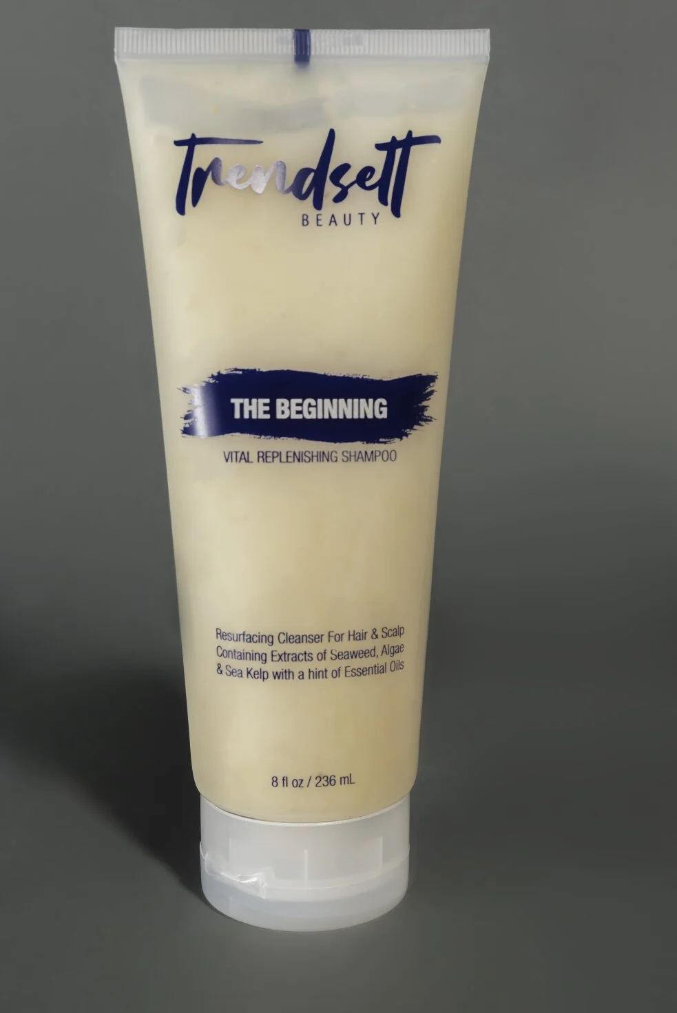 Bottle of Trendsett Beauty The Beginning Vital Replenishing Shampoo containing seaweed, algae, sea kelp, and essential oils, with 8 fl oz volume, placed on a dark gray surface.