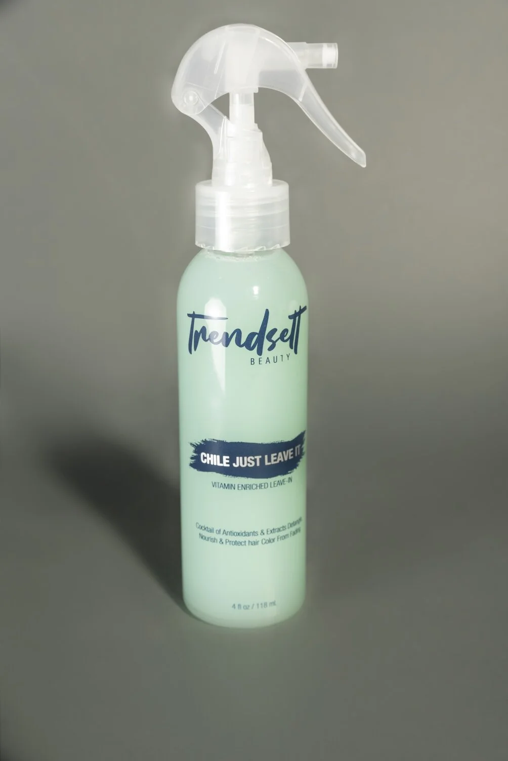 A light green spray bottle labeled 'Trendsett Beauty' with the slogan 'Chile Just Leave It,' containing a leave-in hair product.