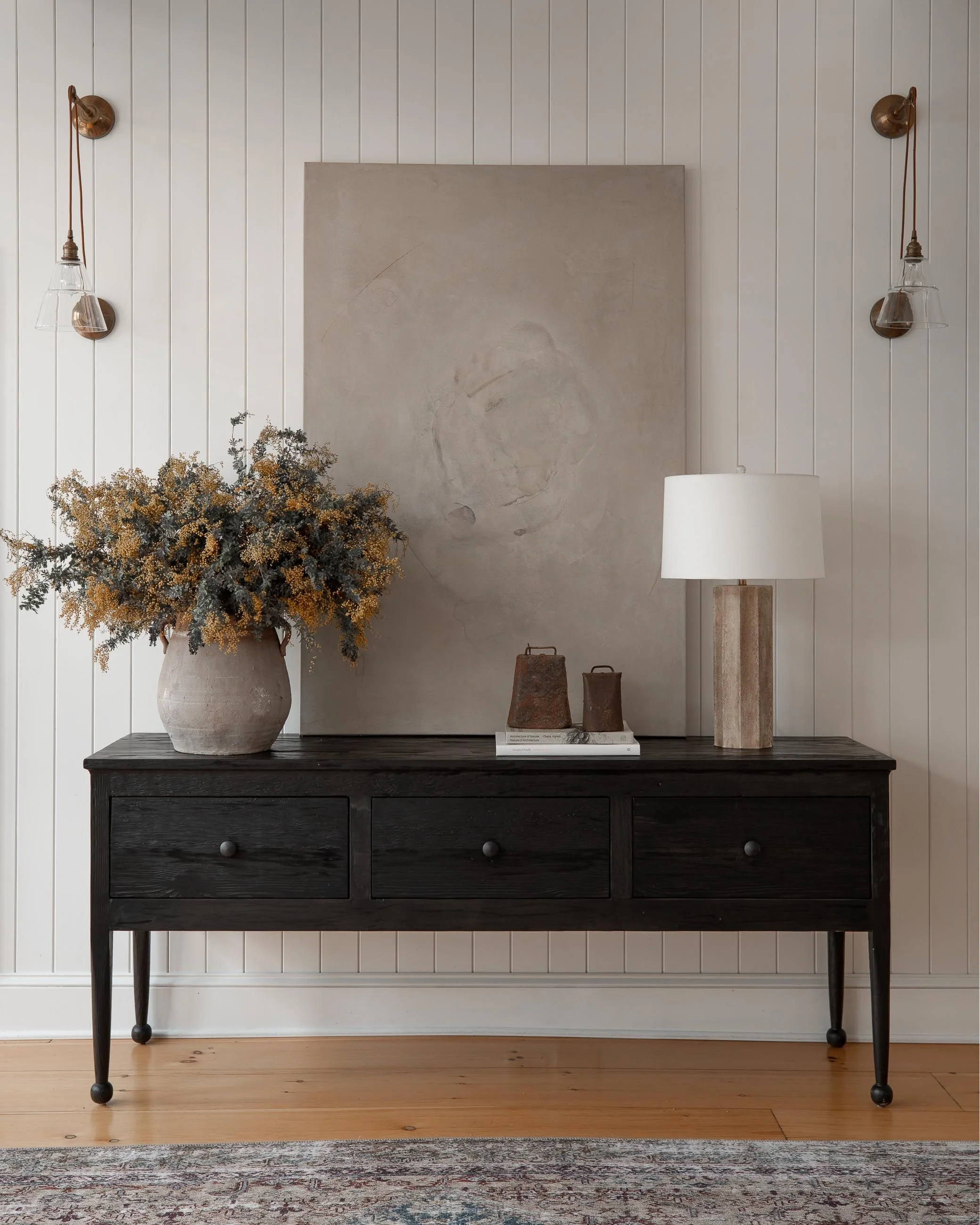 Sophisticated console table setup with pendant lights, autumnal flora, and an abstract artwork