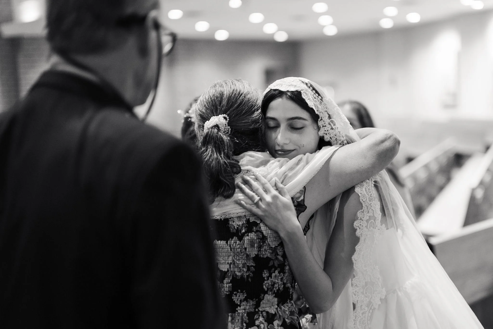 A young woman in a wedding dress and veil embraces an older woman with gray hair and a patterned dress in a emotional hug at St. Mathews Catholic Church in Charlotte.