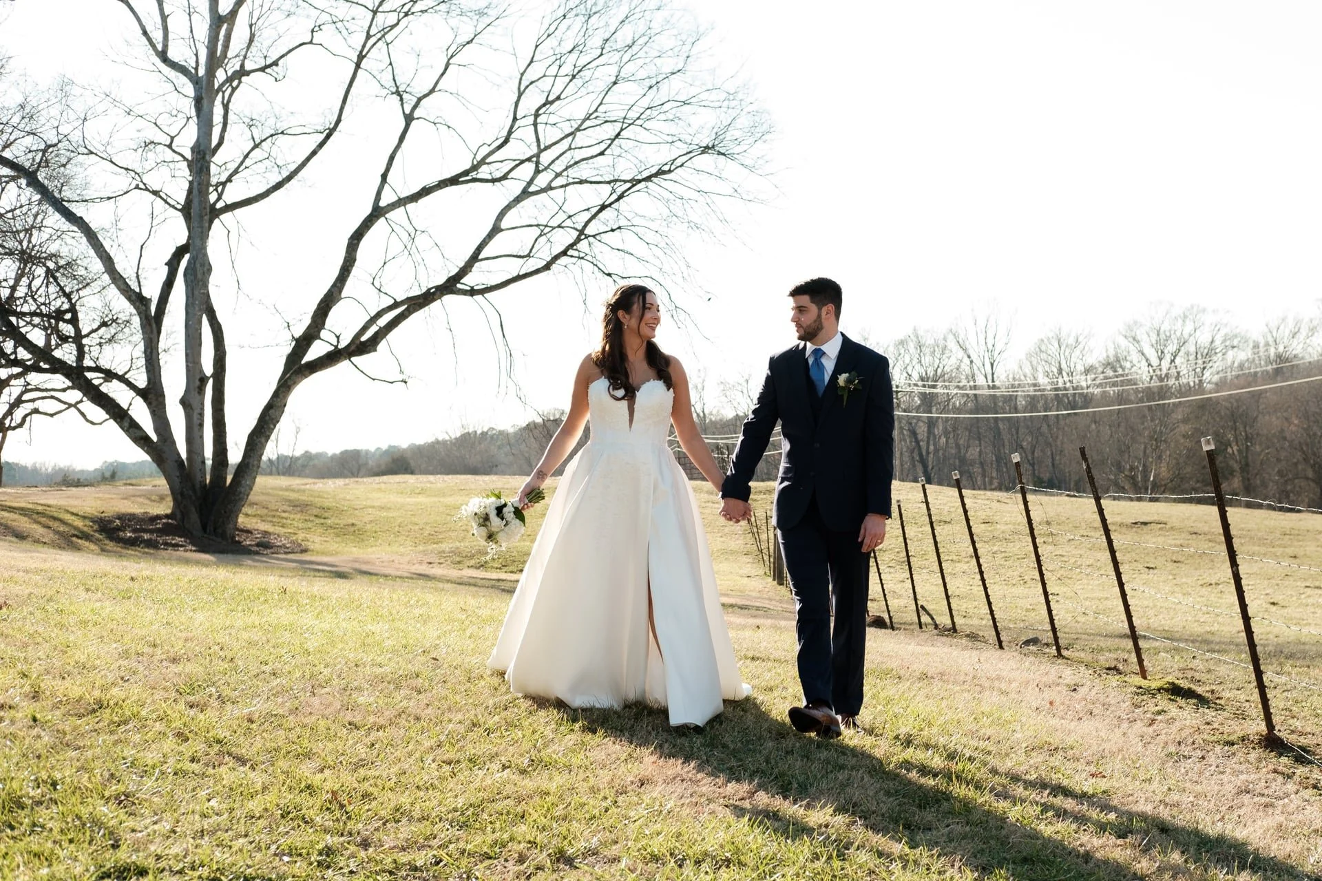 bride and groom holding hands and walking in a green field near Founders Dairy Barn