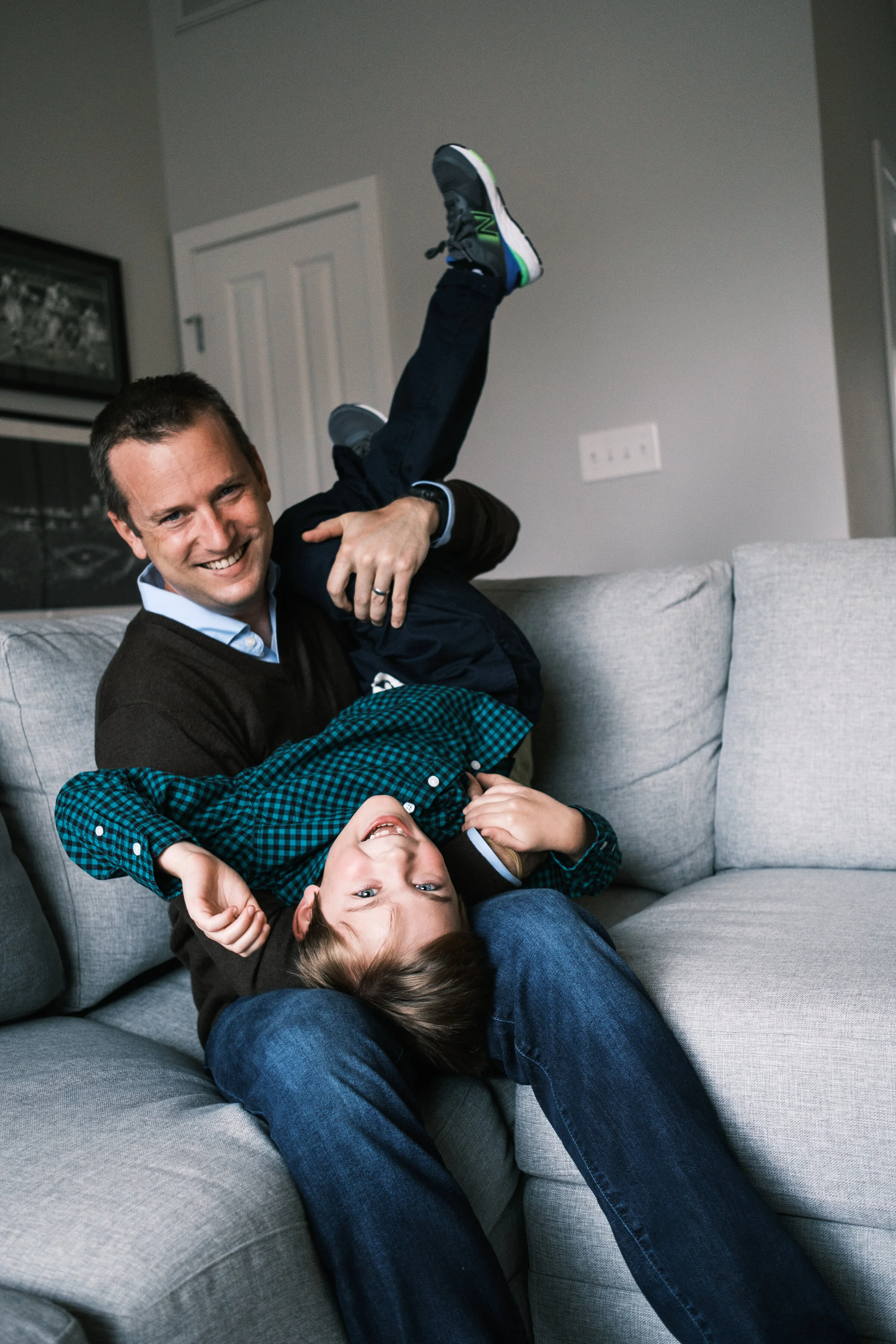 father and son laughing on the couch.Son appears to be upside down and smiling at the camera