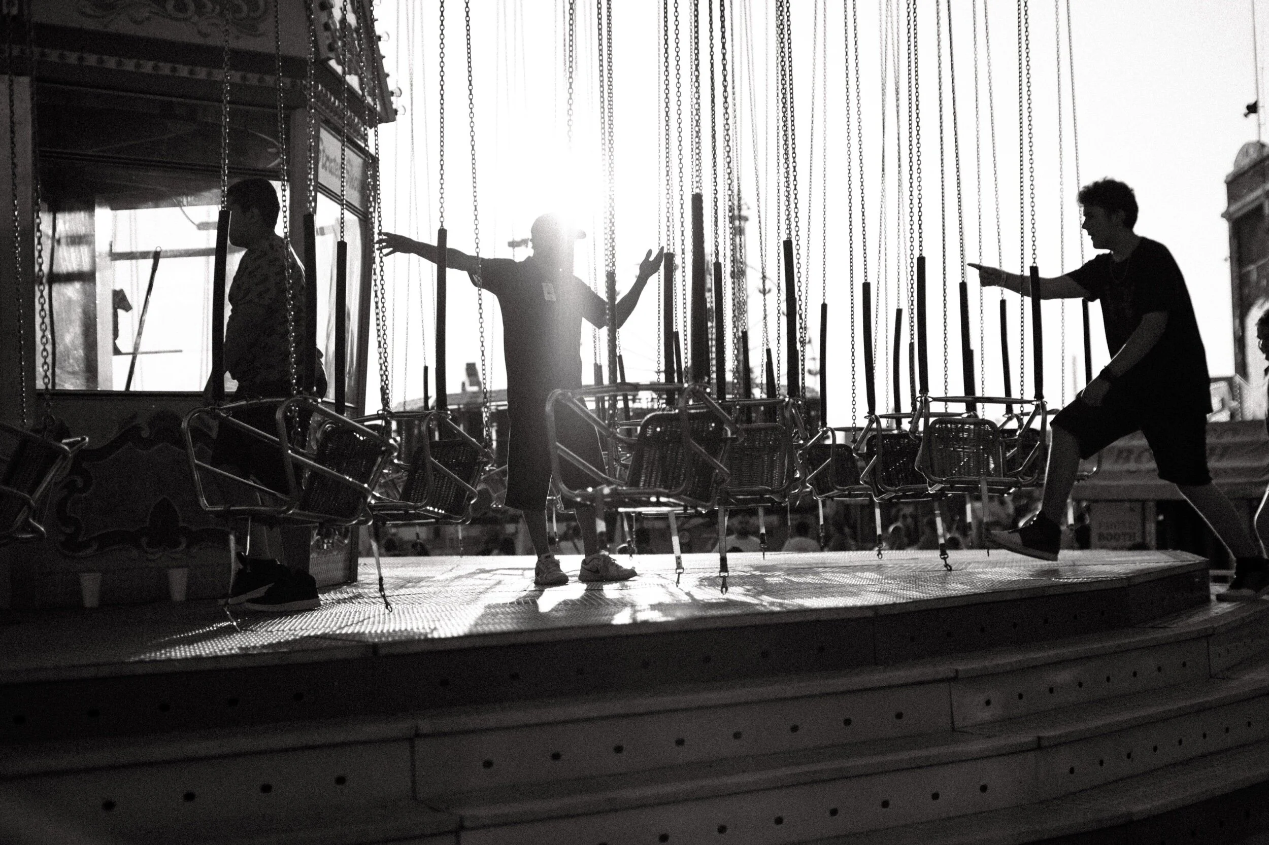 Silhouettes of people arranging swing chairs on a carousel at a carnival with sun shining through.