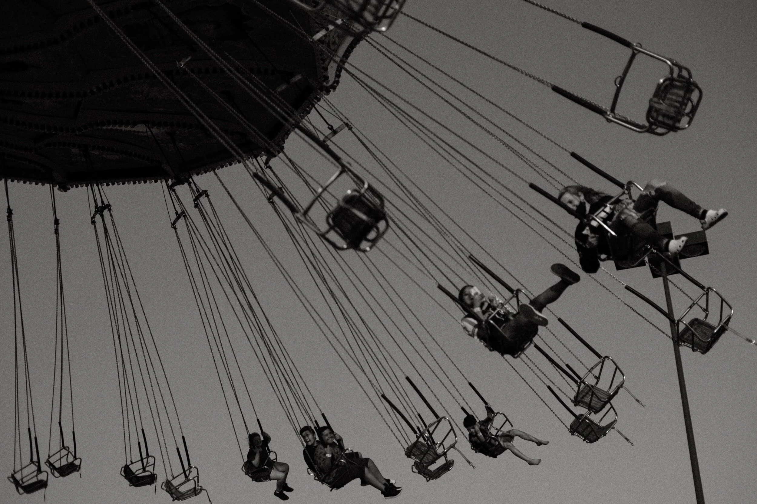 Black and white photo of a swing ride at an amusement park with people seated and swinging through the air.
