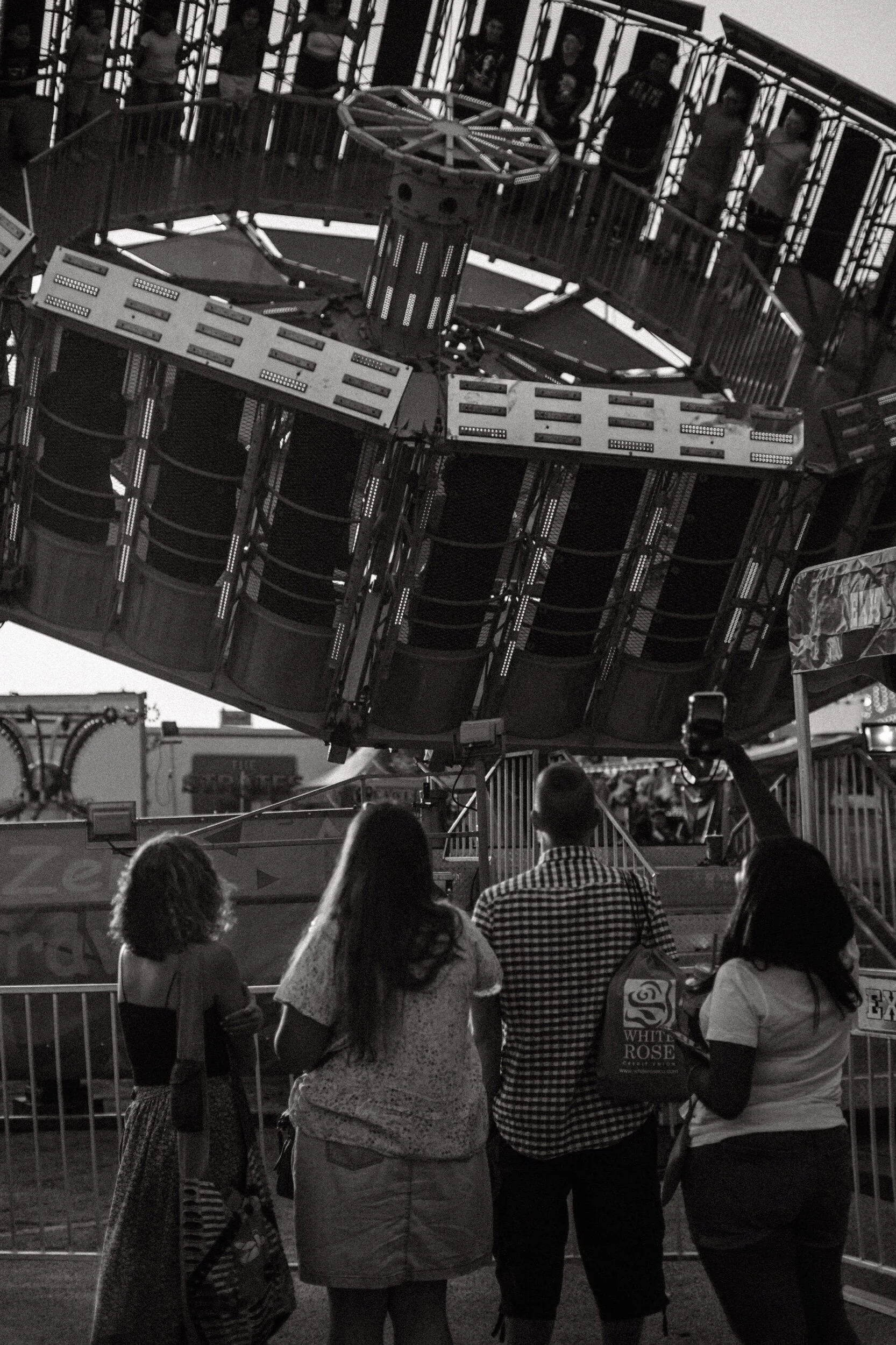 People watching a spinning carnival ride at an amusement park.