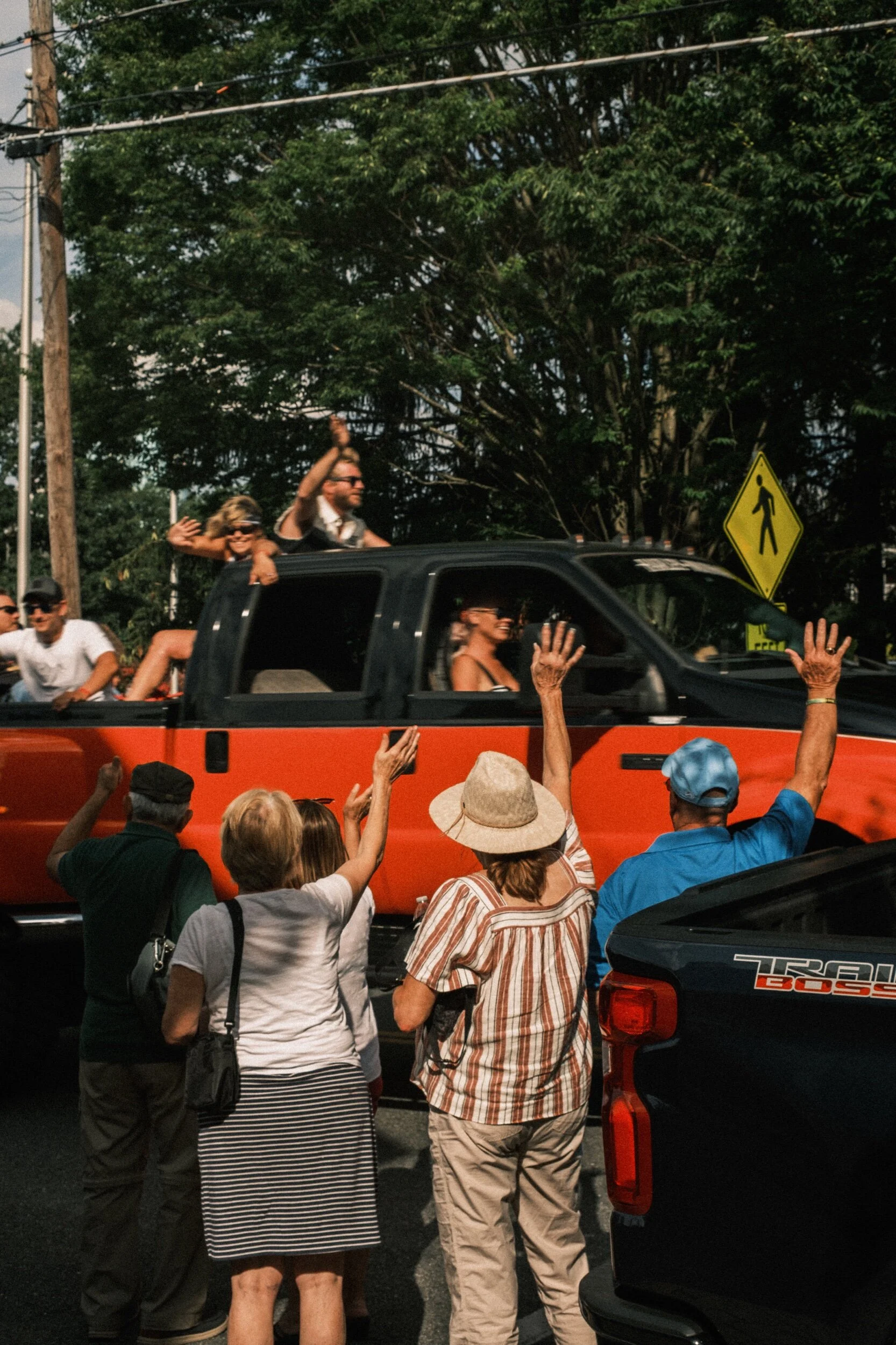 People waving from and at a red pickup truck on a street.