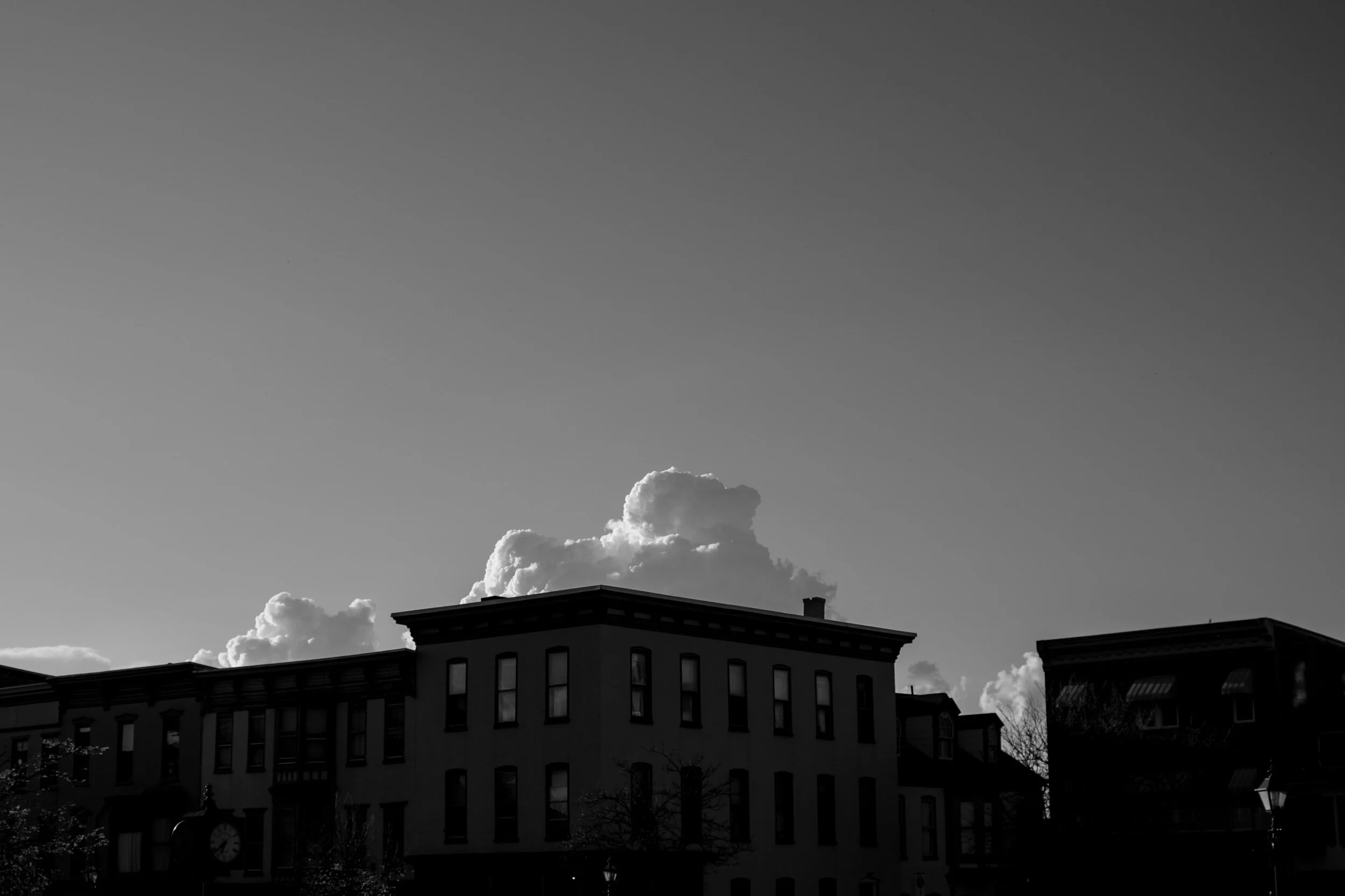 Black and white image of row houses with large clouds in the sky above.