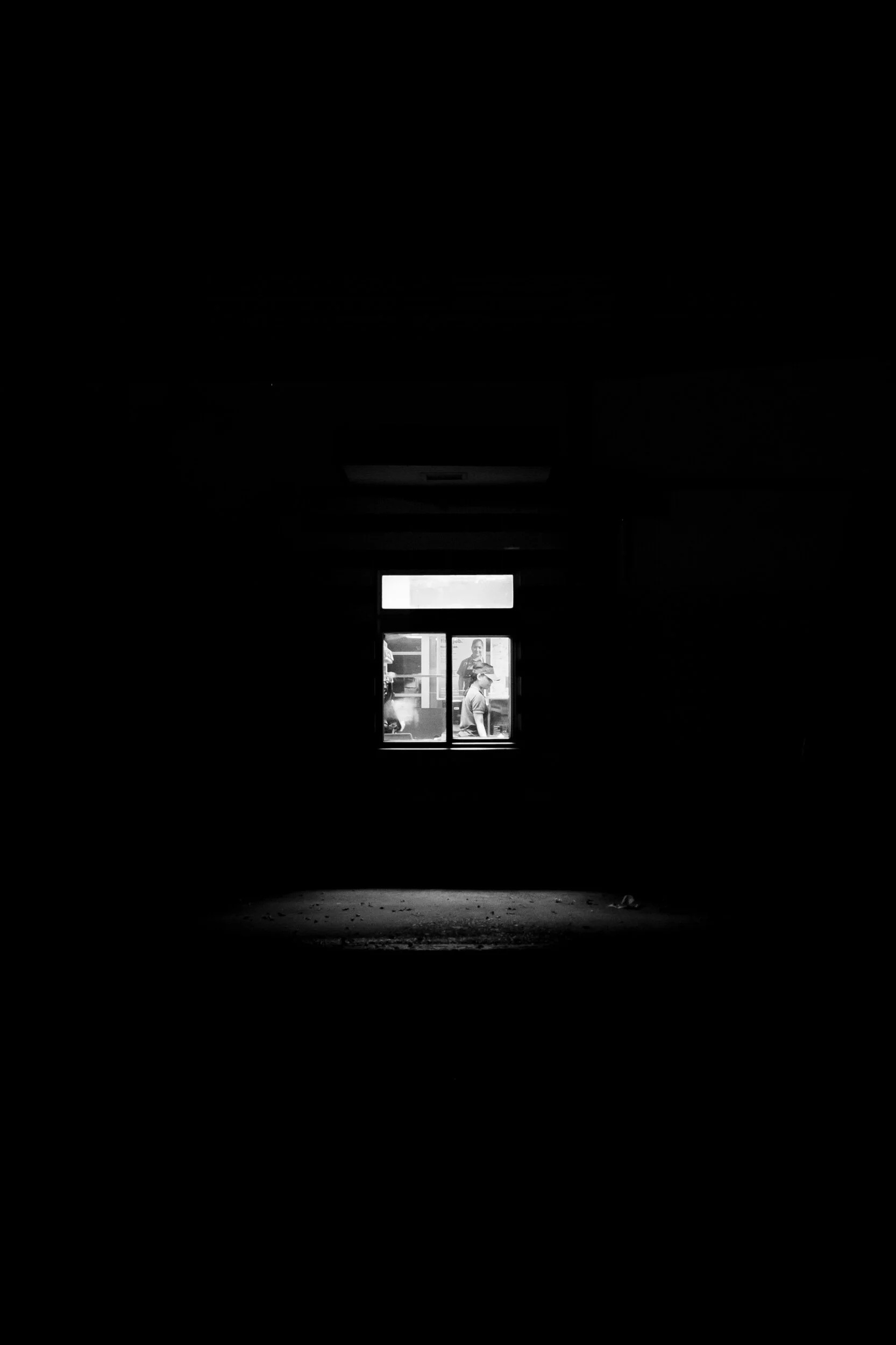 Silhouette of people visible through a window in a dark room with a spotlight on the floor.