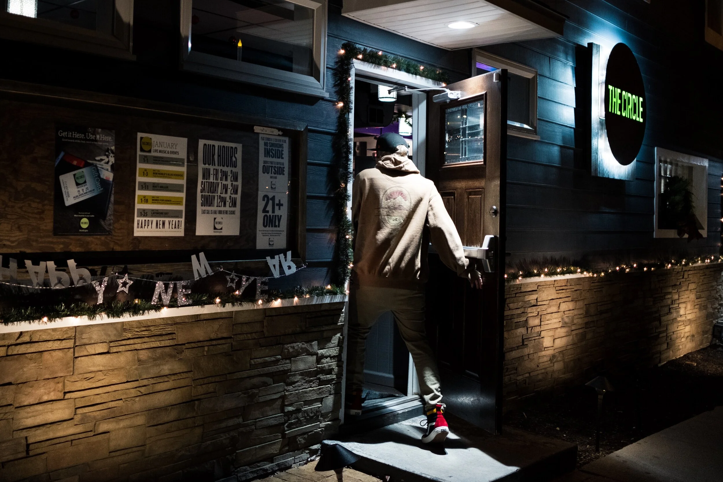Person entering a bar called The Circle at night with holiday lights and decorations outside.