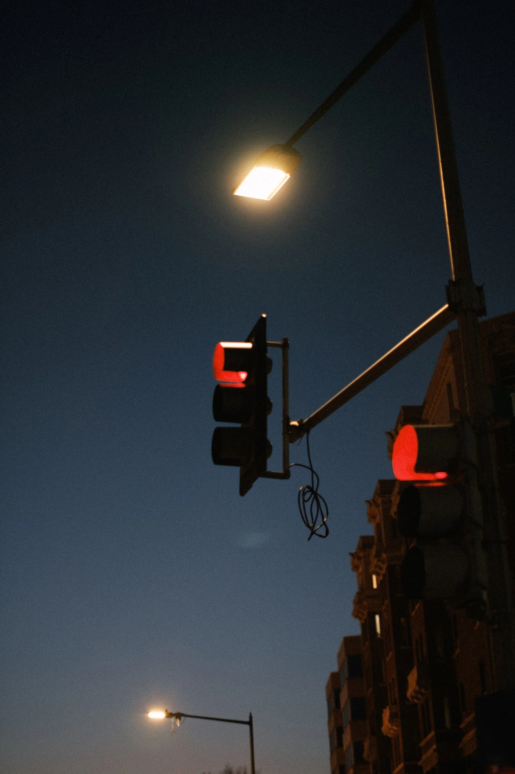 Traffic light and streetlamp at dusk with building in the background.