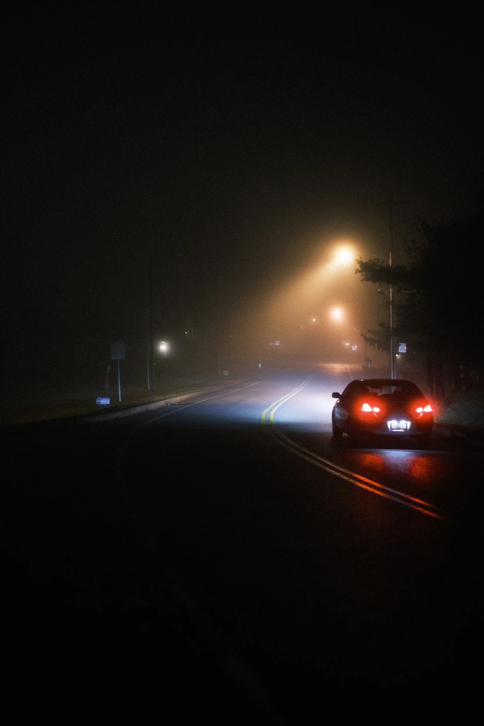 Car driving on foggy road at night under streetlights