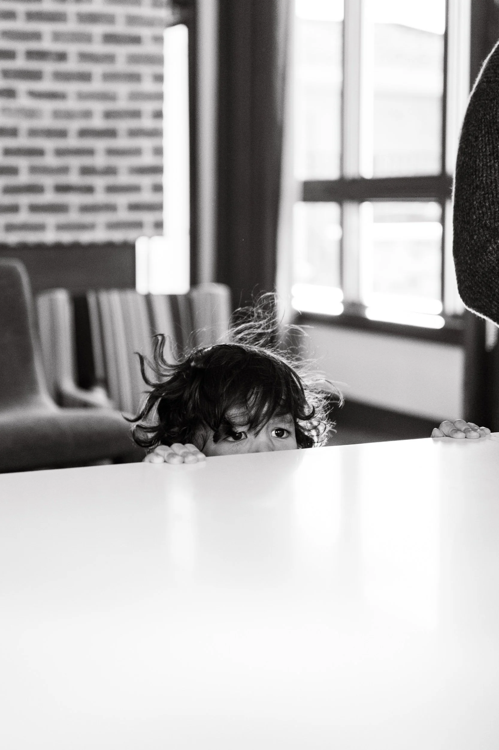 black and white photo of a toddler with messy hair,peeking his eyes above a counter top during a documentary family photo session in Charlotte